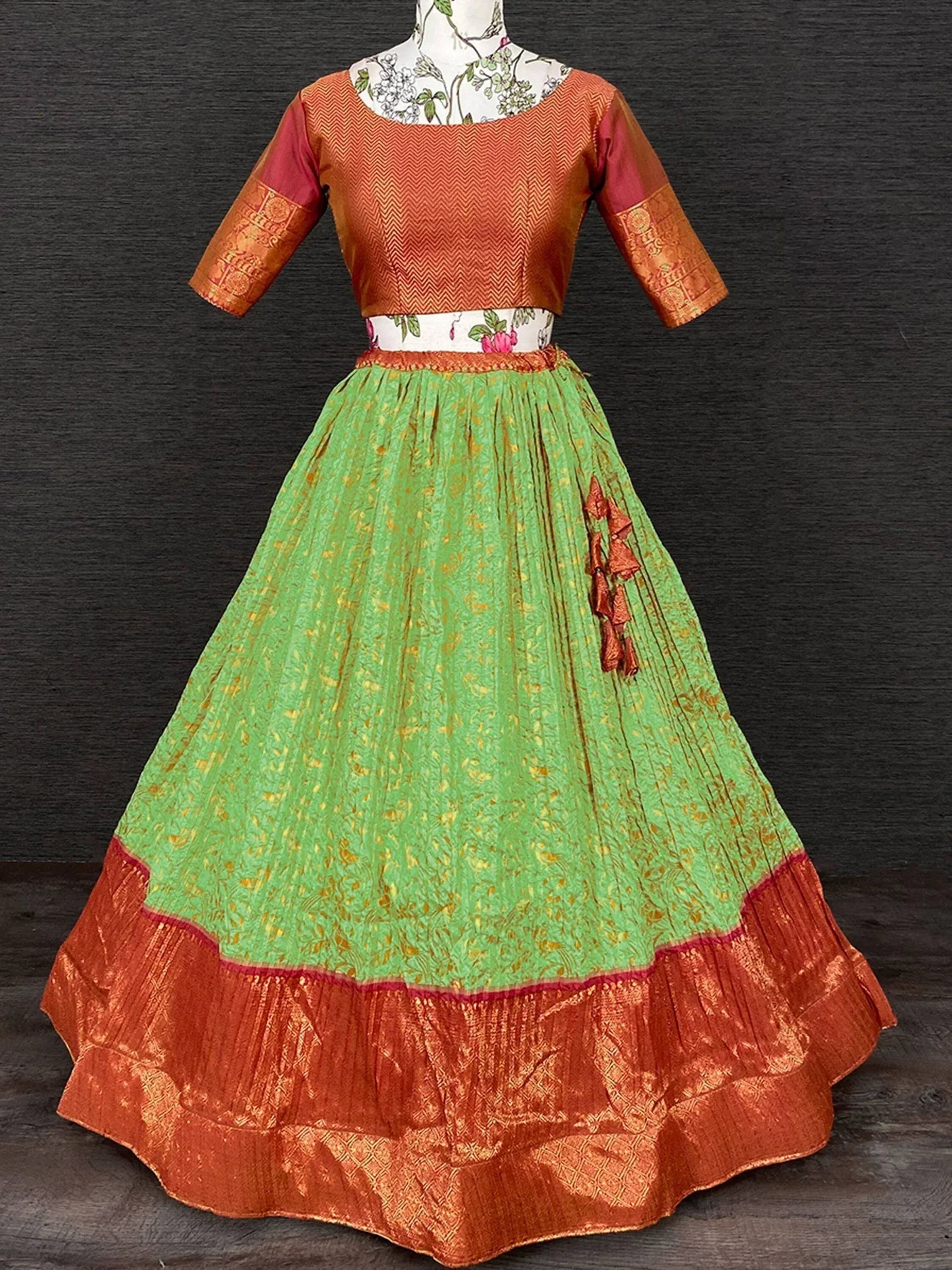 Green and orange ethnic lehenga choli with floral print and pleated skirt, perfect for Indian festivals and weddings.