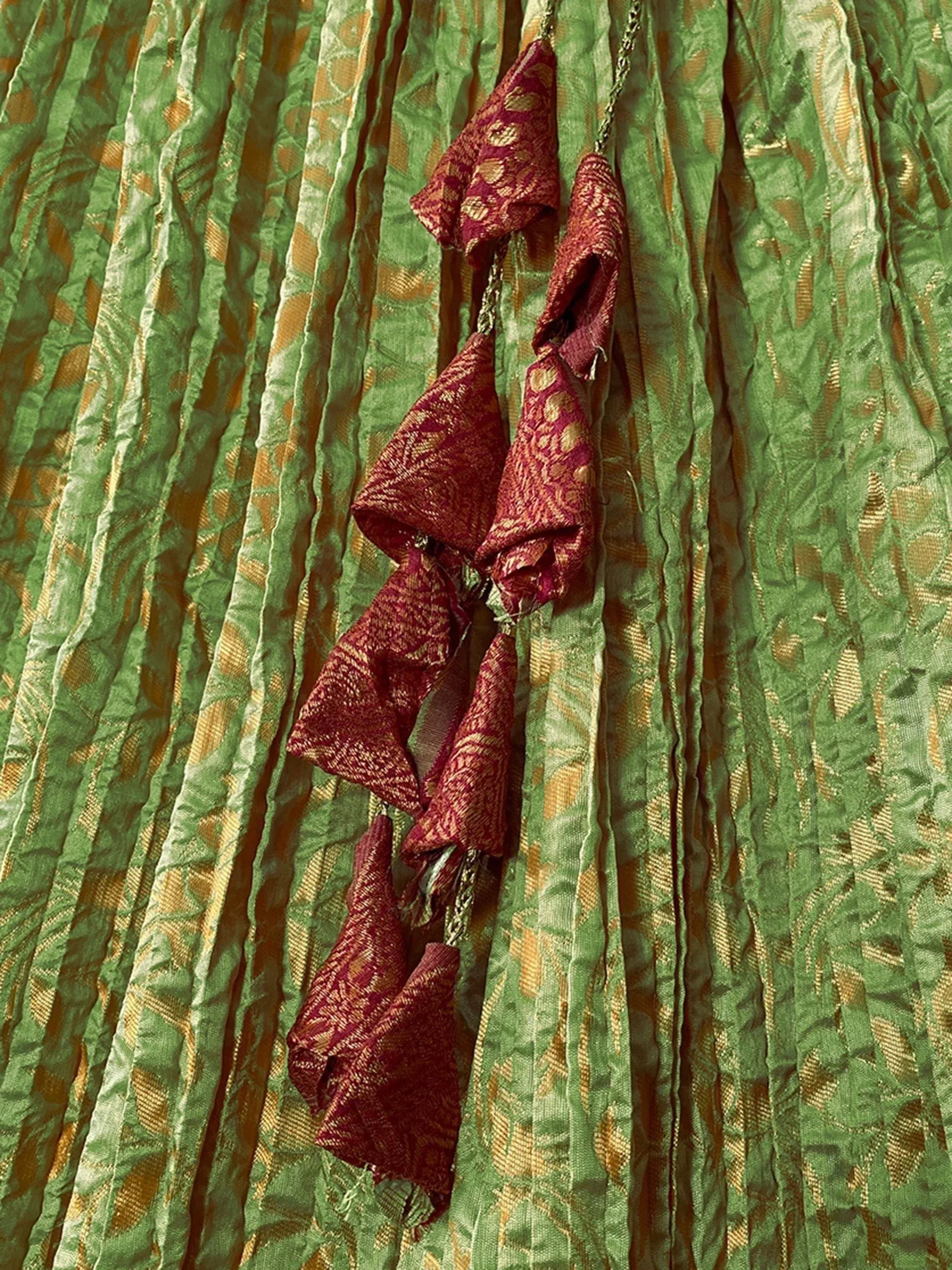 Green and gold pleated ethnic skirt with maroon tassel detailing, perfect for Indian wear.