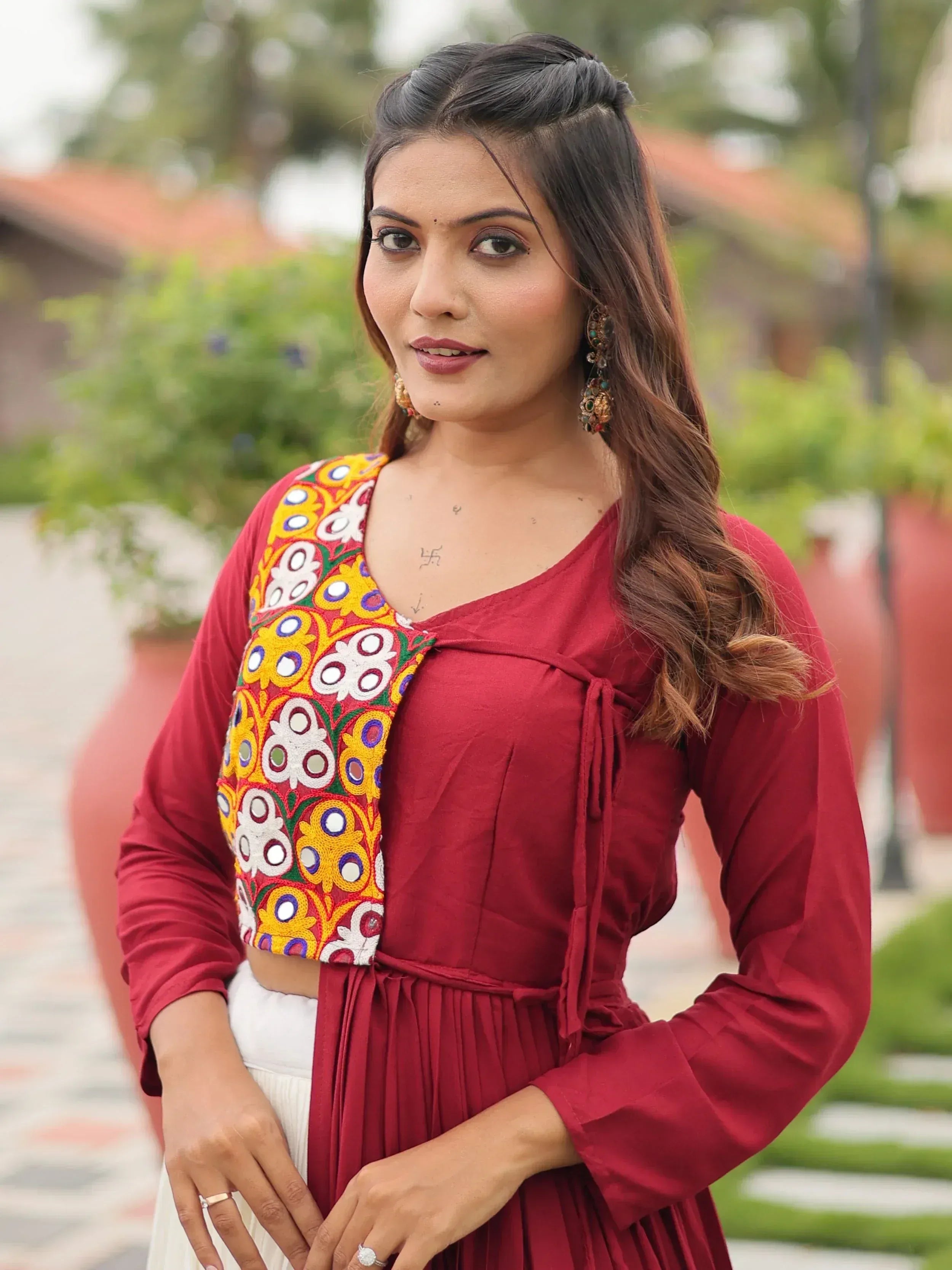 Woman in maroon ethnic kurta with colorful mirror embroidery, paired with white palazzo, outdoor setting