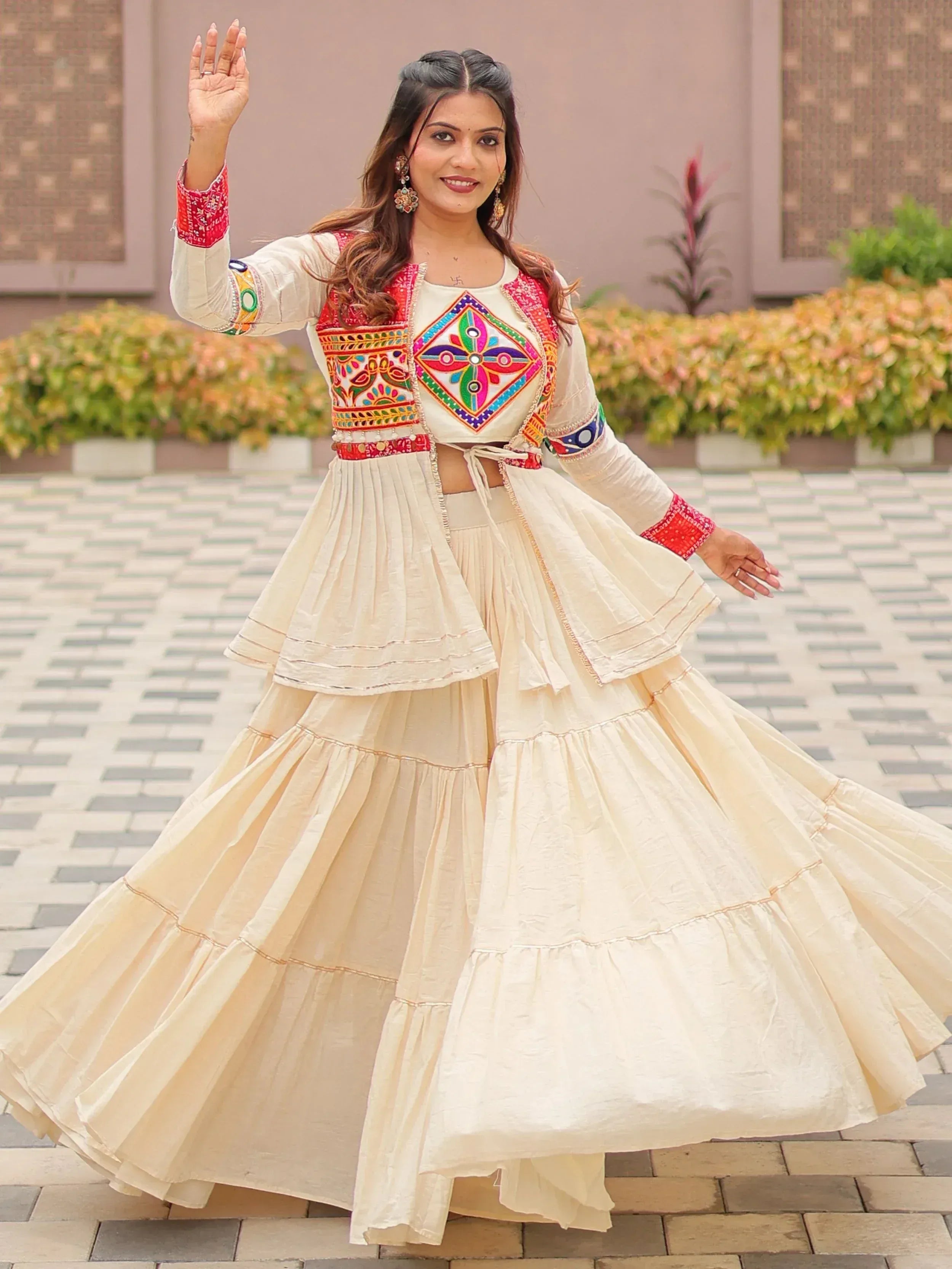 Woman in cream embroidered lehenga choli with colorful mirror work, twirling outdoors