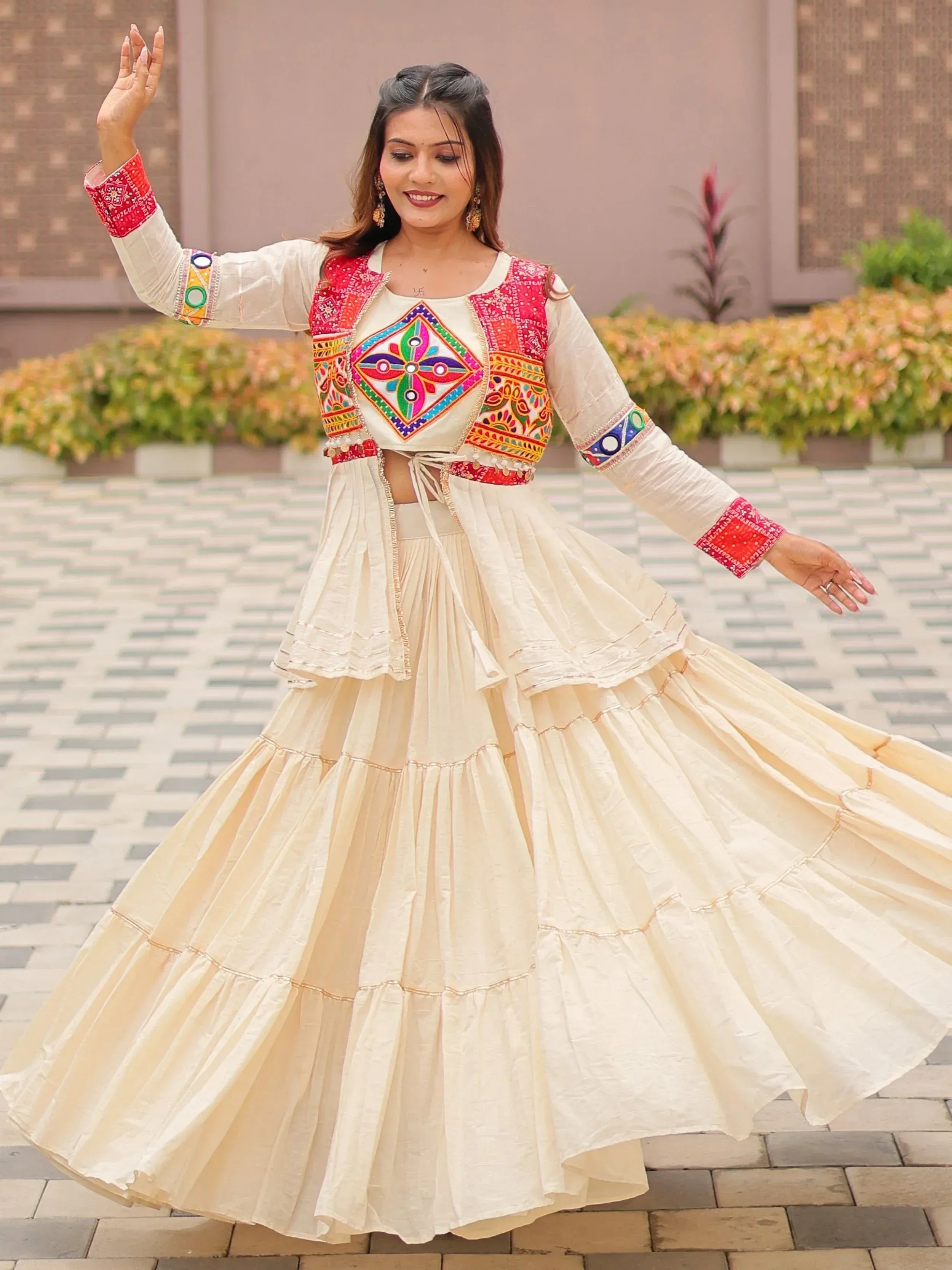 Woman in cream embroidered lehenga choli with colorful mirror work, twirling outdoors