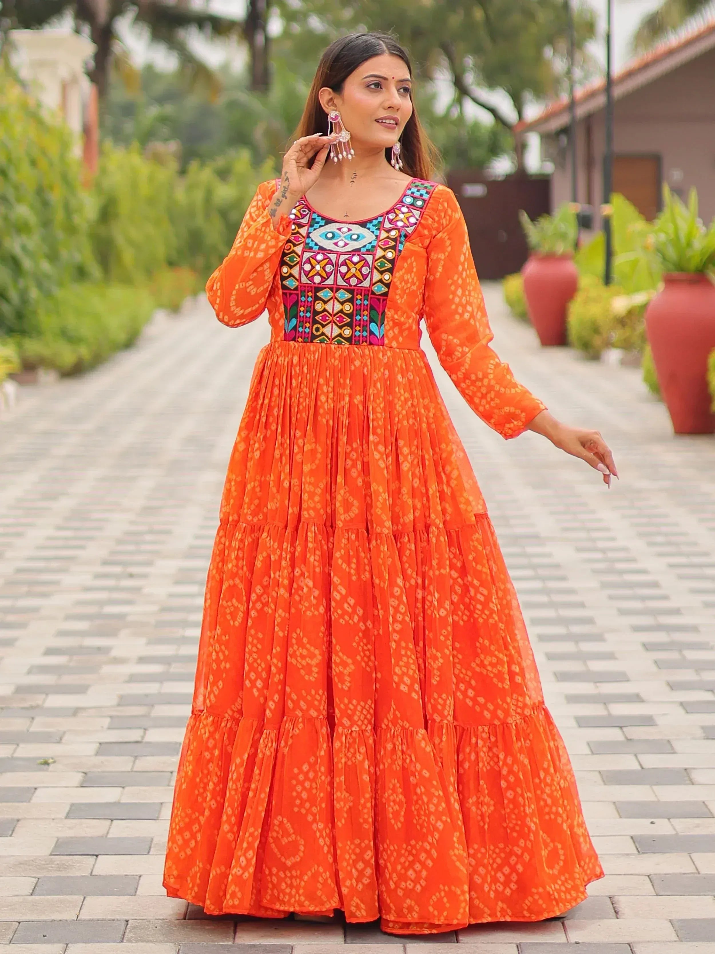 Vibrant orange ethnic gown with colorful mirror work and tiered skirt, perfect for Indian occasions