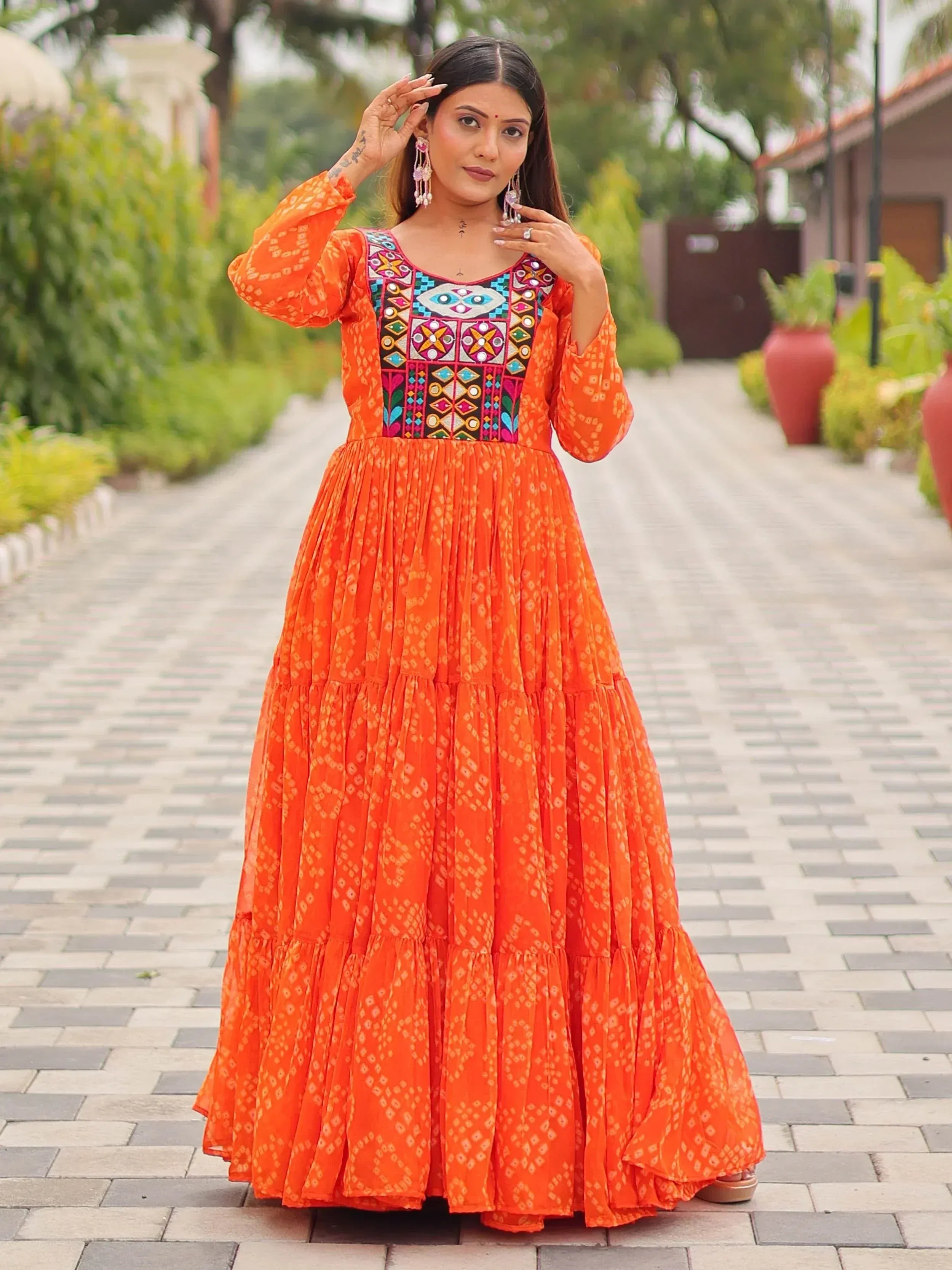 Orange ethnic gown with colorful mirror work and tiered skirt, perfect for Indian occasions
