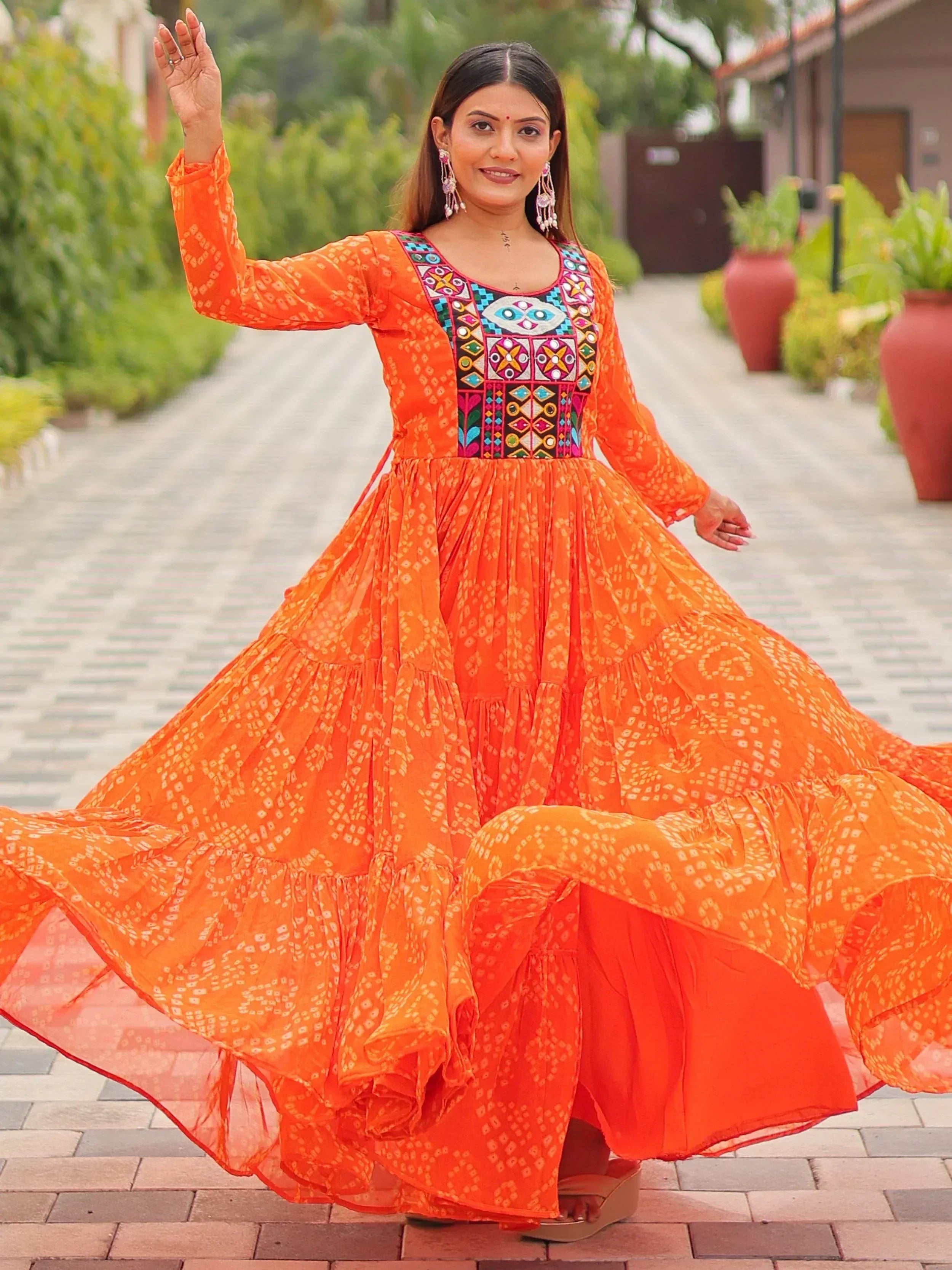 Woman in vibrant orange ethnic gown with colorful embroidery, twirling outdoors