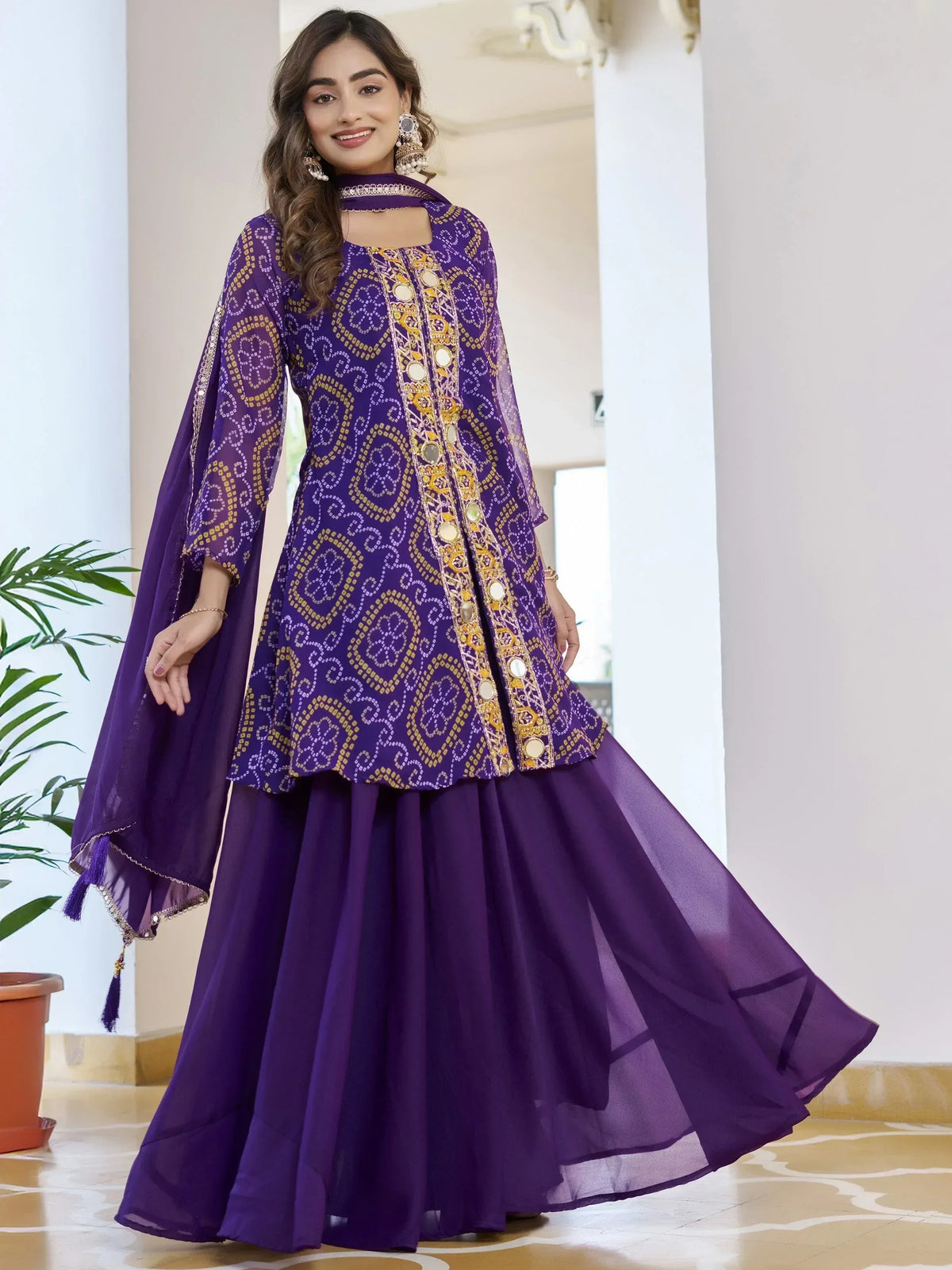 Purple ethnic gown with gold embroidery and mirror work, paired with matching dupatta for festive occasions