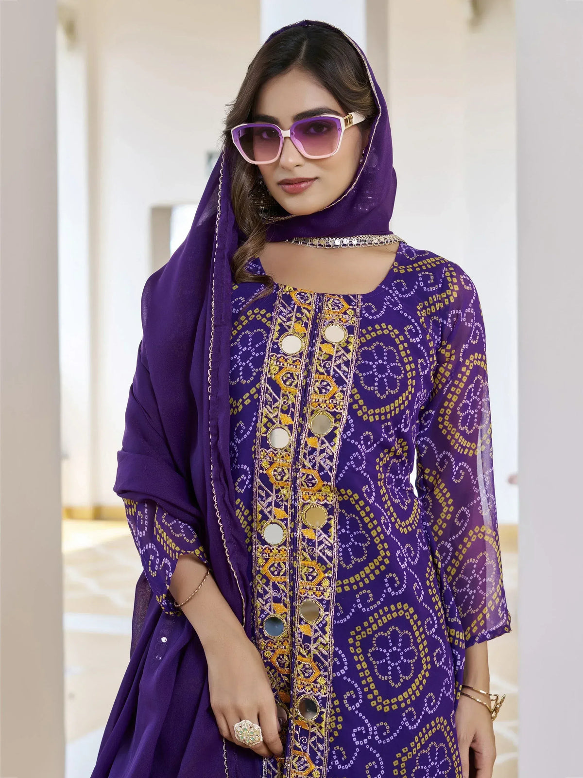 Purple ethnic kurta with mirror work and gold embroidery, paired with matching dupatta and sunglasses