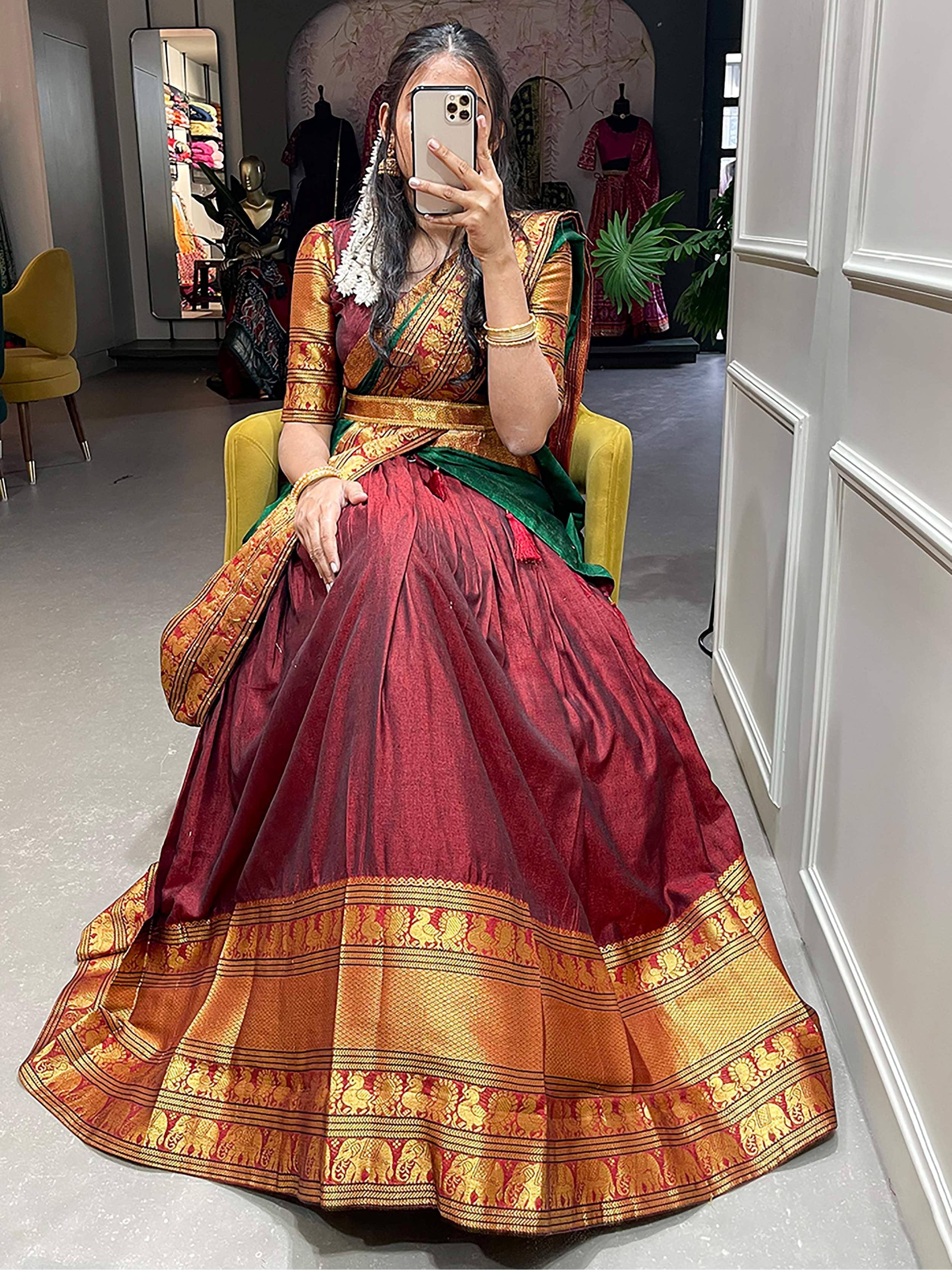 Woman in maroon and gold designer lehenga choli with green dupatta, taking mirror selfie in boutique