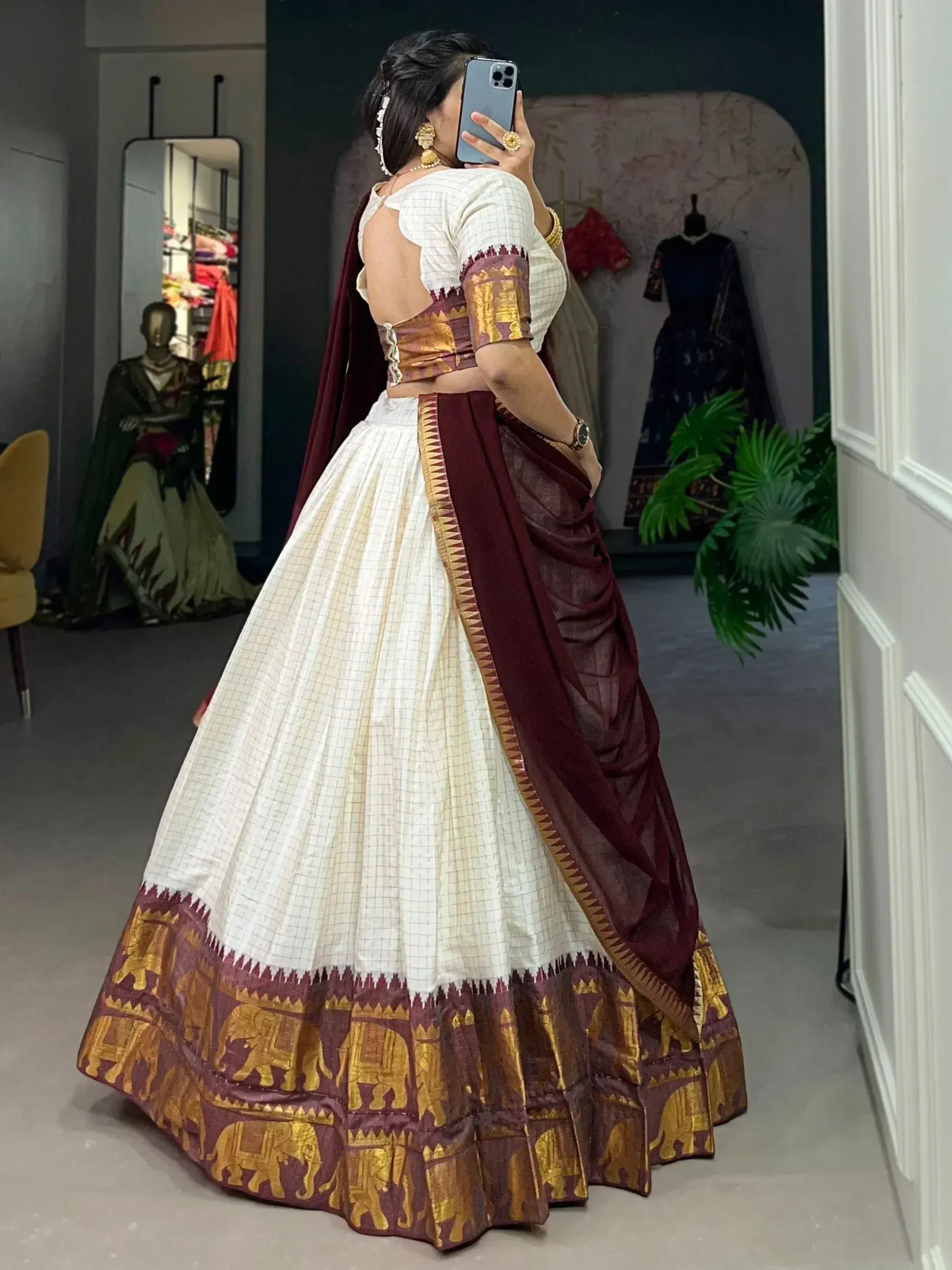 Woman in white and maroon ethnic lehenga with gold elephant print, backless blouse, mirror selfie in boutique