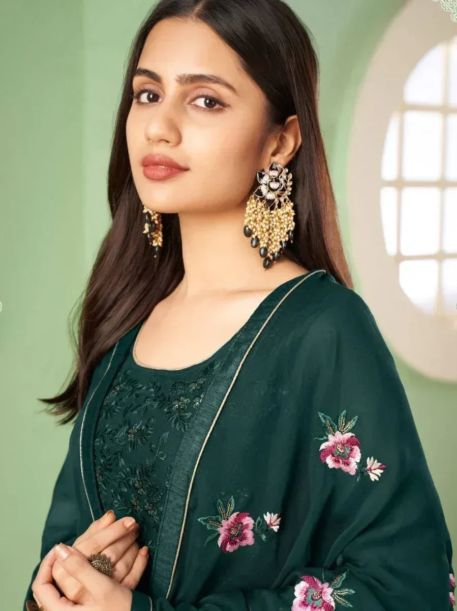 Woman in dark green embroidered salwar kameez with floral details and statement earrings