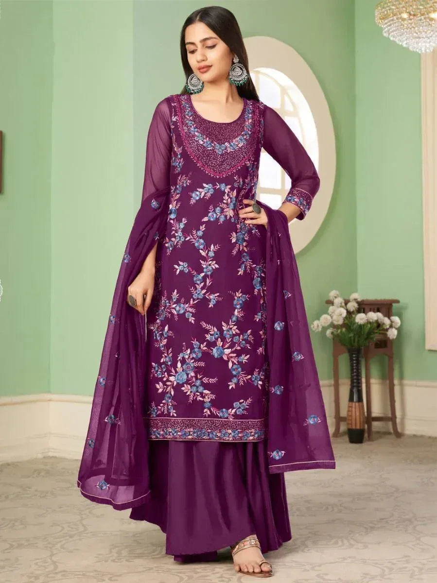 Woman in a purple floral embroidered salwar kameez with dupatta, standing indoors