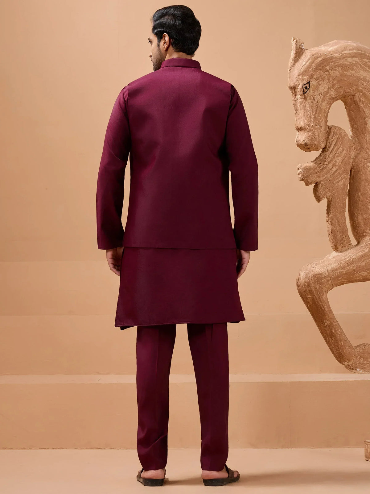 Man in maroon Indian ethnic kurta set with matching pants, back view near wooden horse sculpture