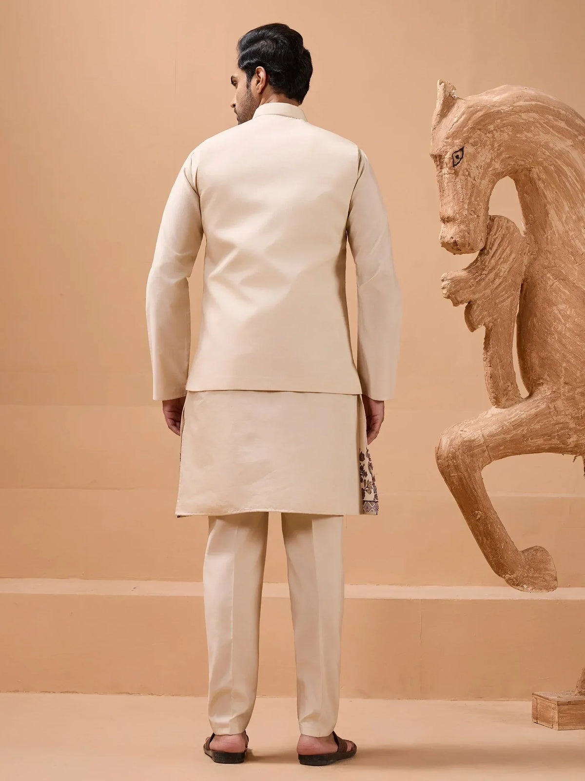 Beige men's kurta set with embroidered hem, paired with matching pants and jacket, styled for ethnic occasions.
