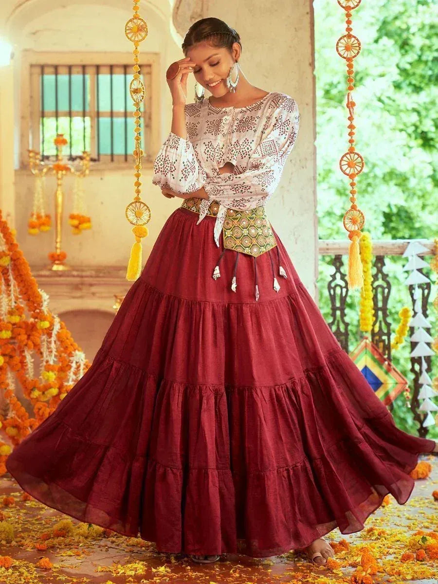 Woman in maroon tiered skirt and embroidered blouse, festive Indian ethnic wear with floral decor
