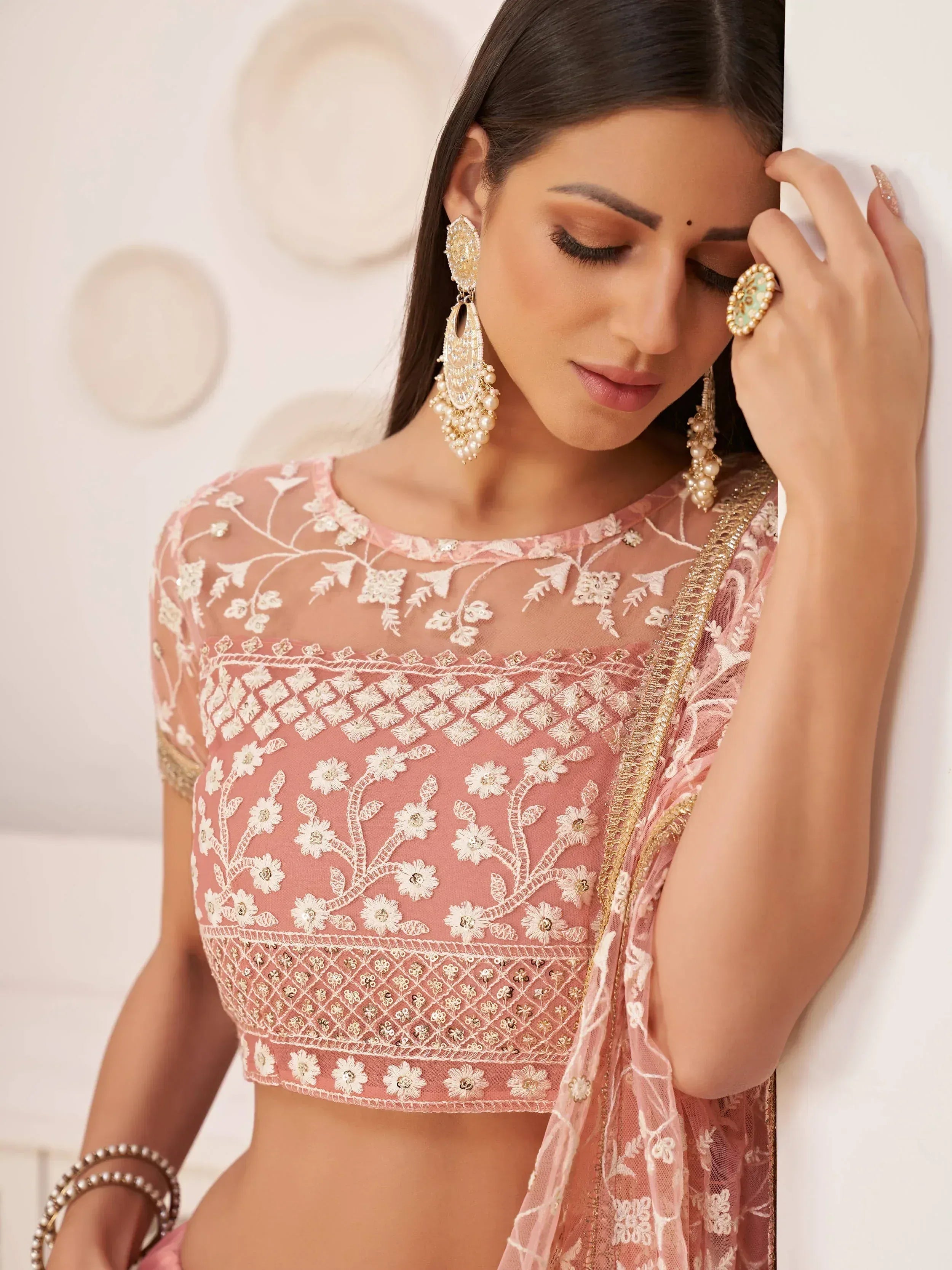Pink embroidered lehenga choli with floral lace and gold detailing, paired with statement earrings