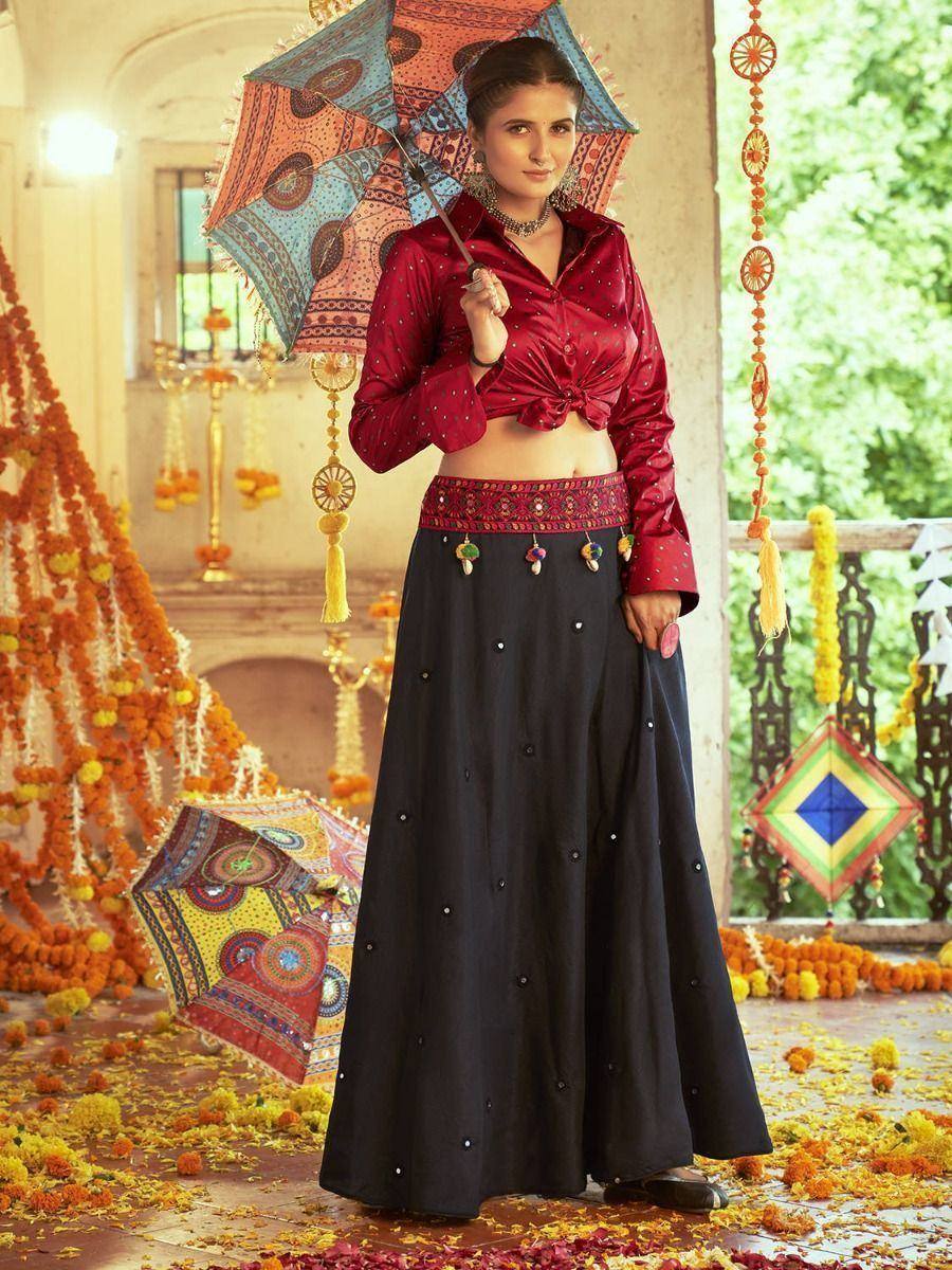 Woman in red embroidered top and black lehenga with floral decor, holding patterned umbrella