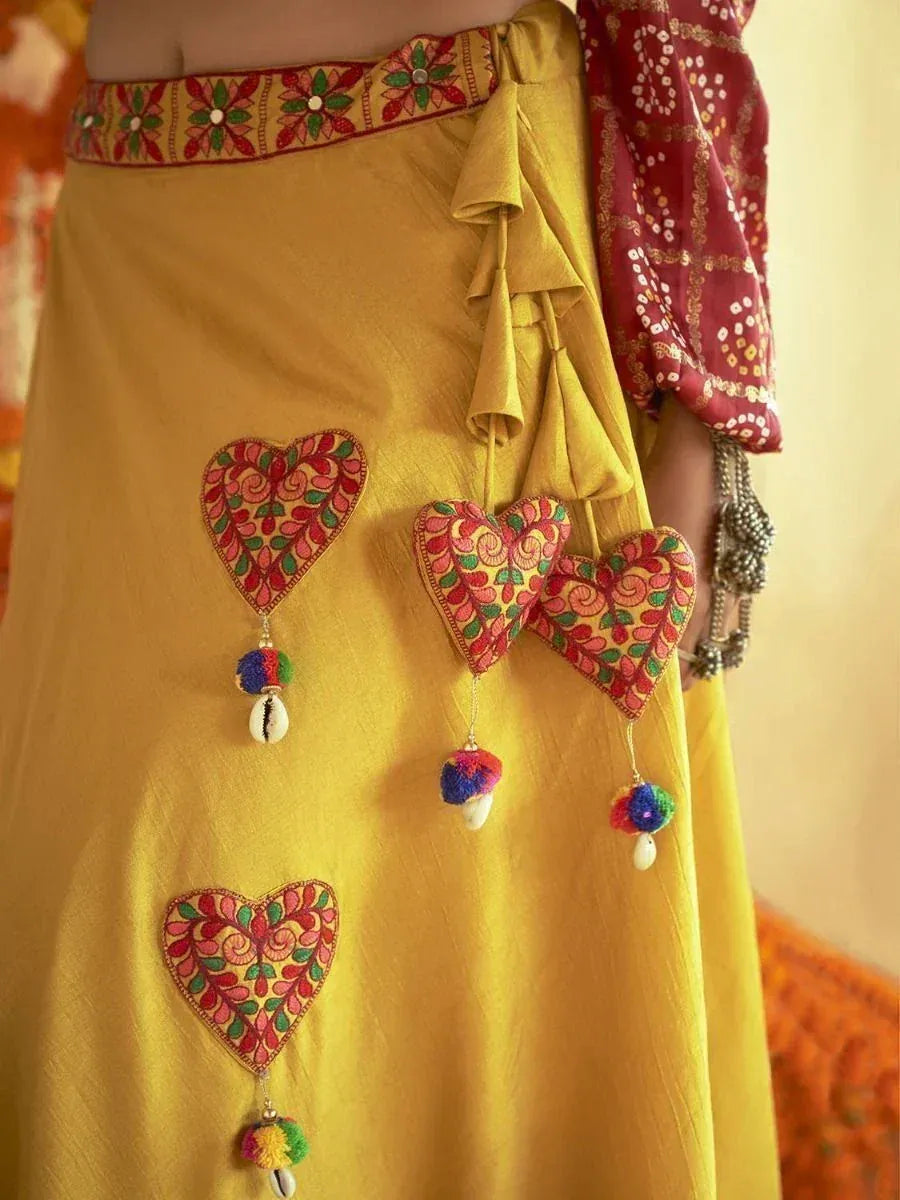 Yellow ethnic skirt with embroidered heart appliqués, pom-poms, and shell charms, paired with red patterned blouse