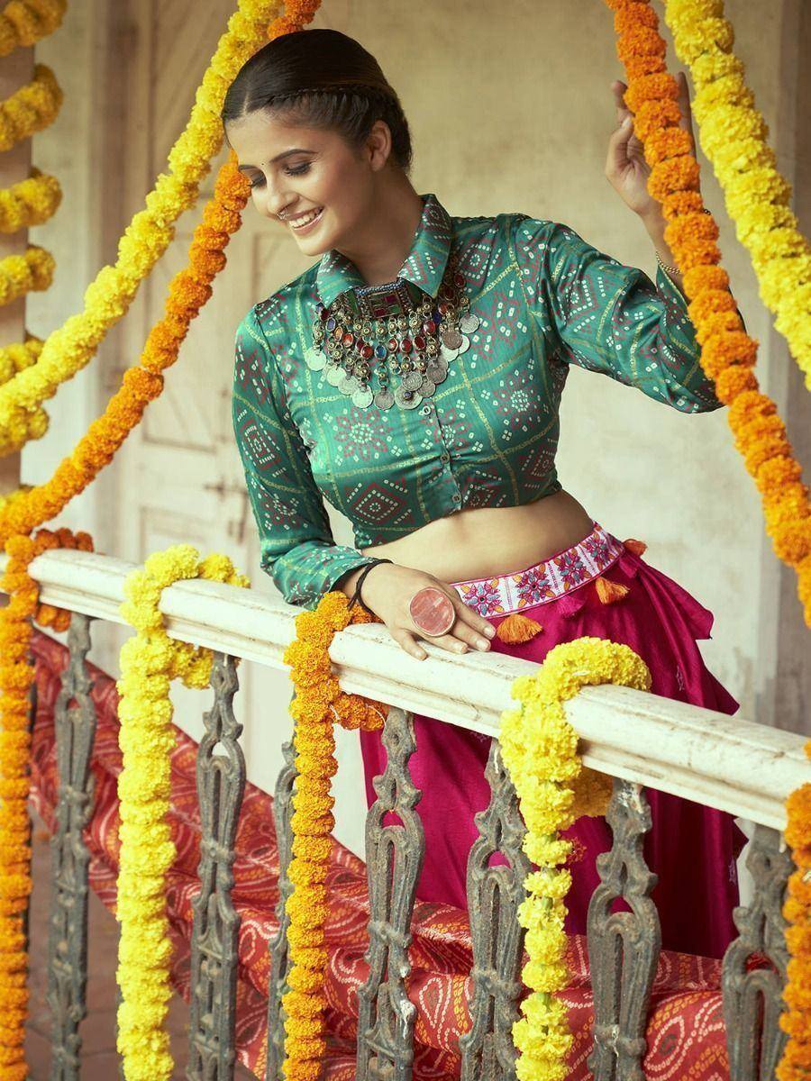 Woman in green printed crop top and magenta lehenga with floral garlands, festive ethnic wear