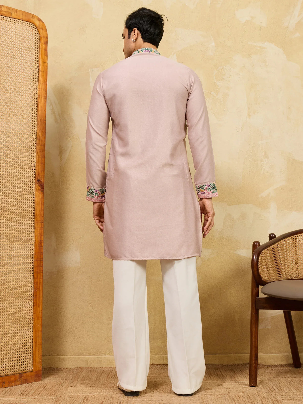 Back view of a man wearing a blush pink embroidered kurta with white wide-leg trousers