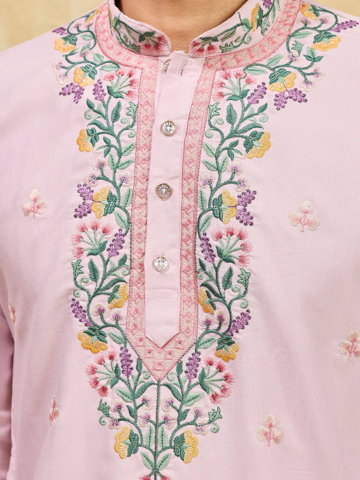 Close-up of a light pink men's kurta with intricate floral embroidery and a button-down placket.