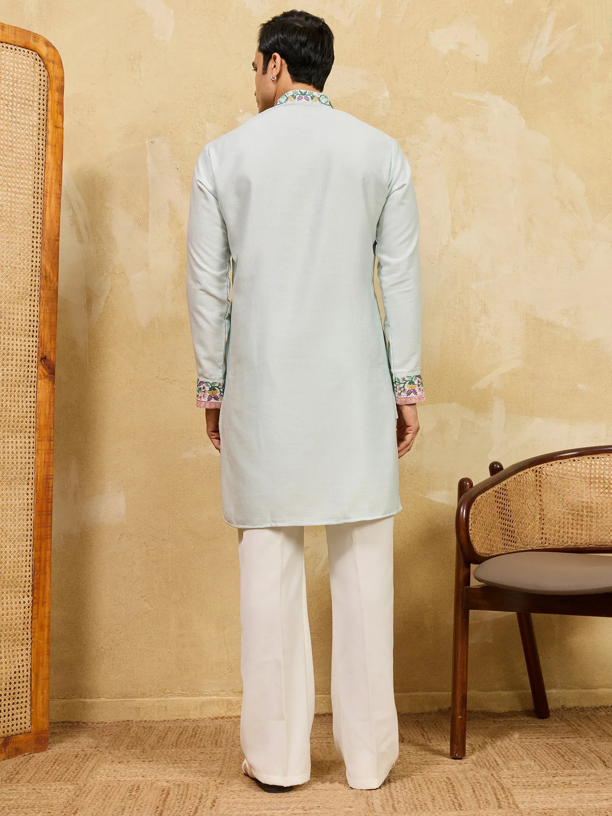 Back view of a man wearing a light blue embroidered kurta and white trousers.