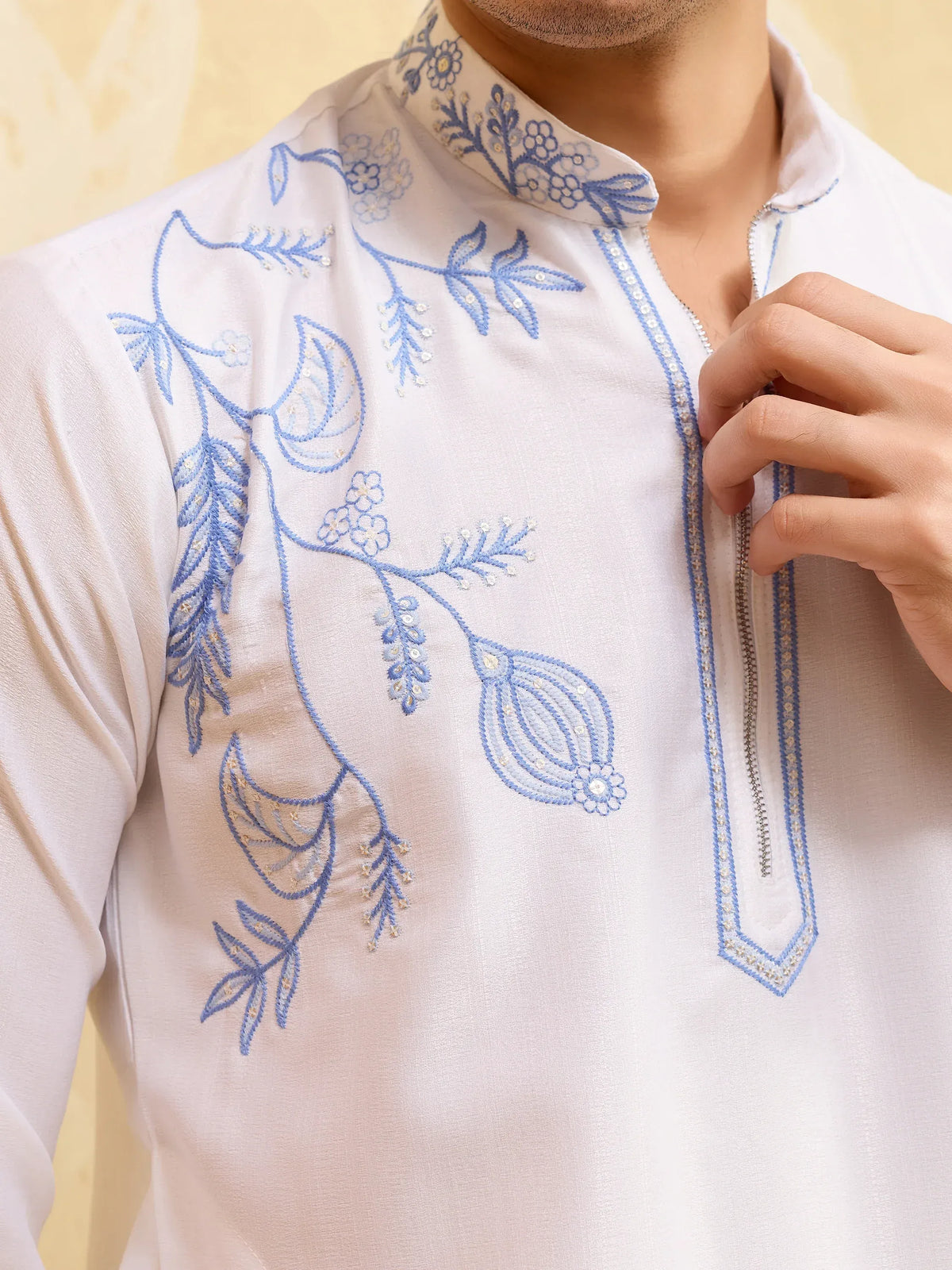 Close-up of a white men's ethnic kurta with blue floral embroidery and sequins.
