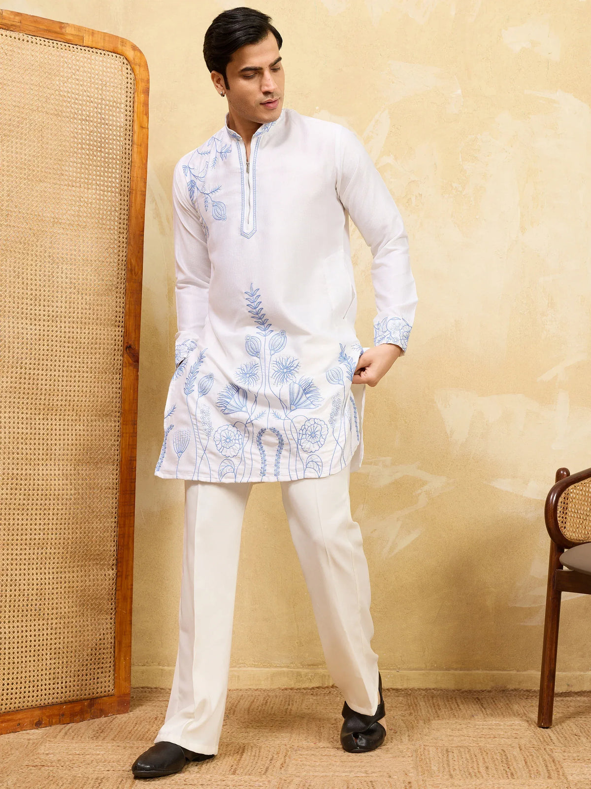 Man wearing a white ethnic kurta with blue floral embroidery and white trousers.