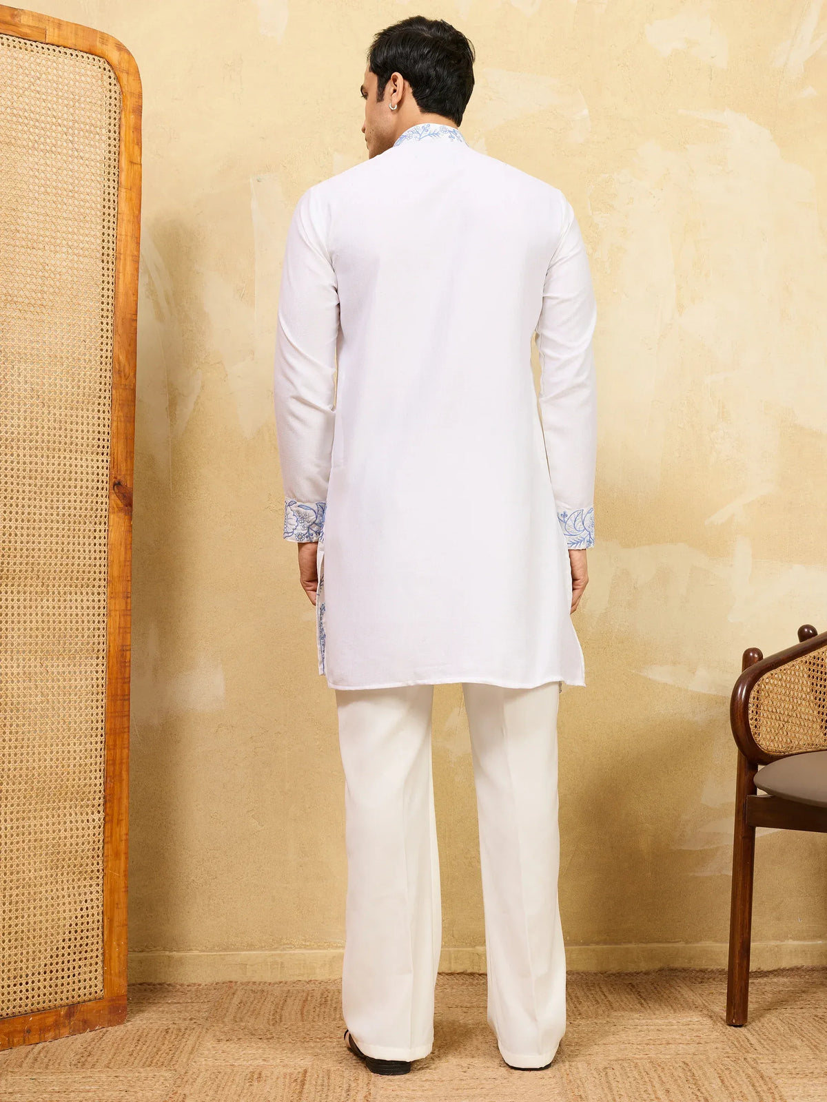 Back view of a man wearing a white ethnic kurta with blue embroidery and matching trousers.