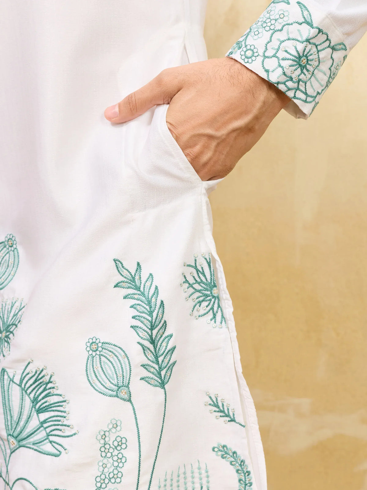 Close-up of a white men's ethnic kurta featuring green floral embroidery and a side pocket.