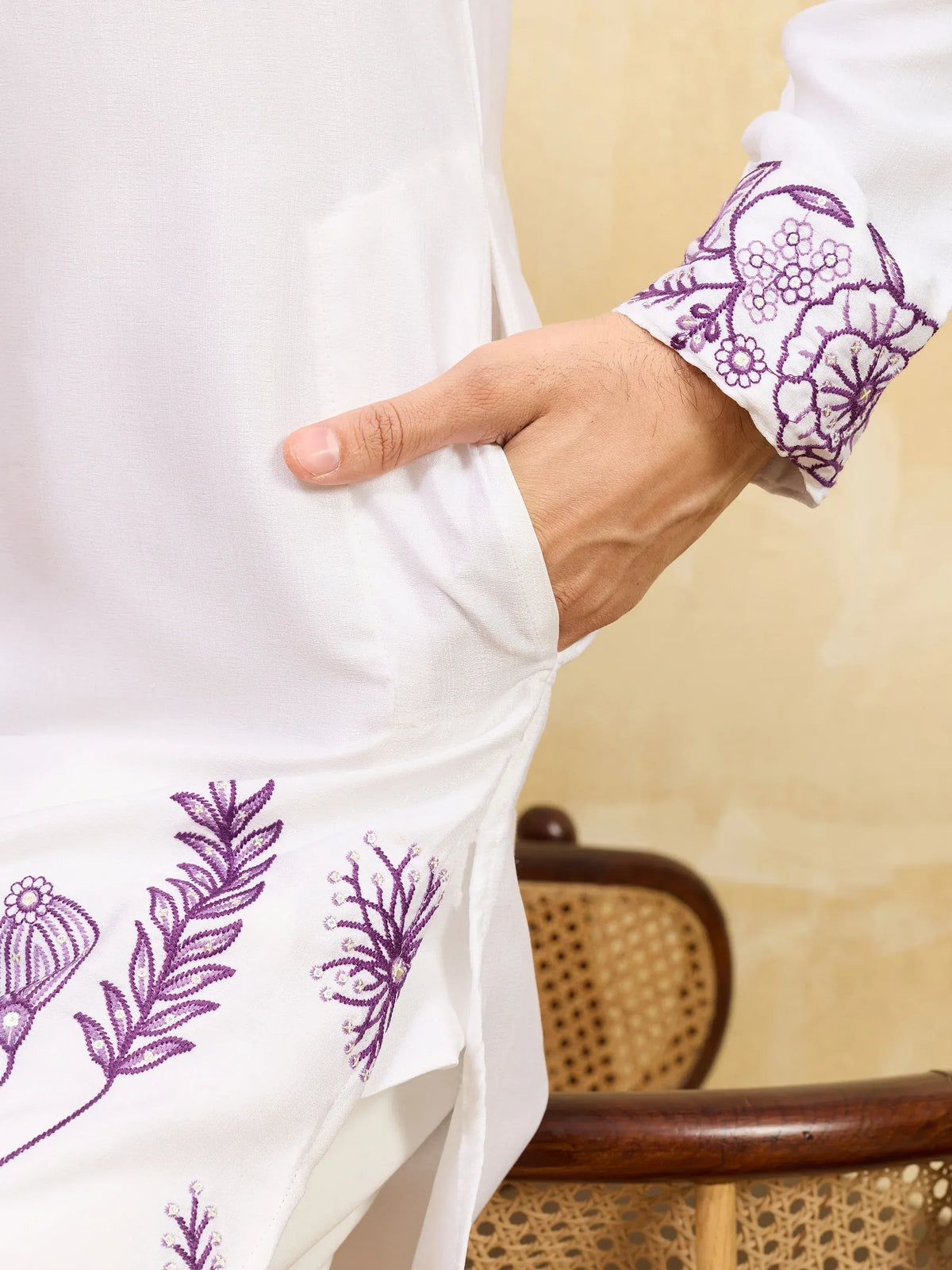 Close-up of a white men's ethnic kurta with purple floral embroidery on the cuff and hem.
