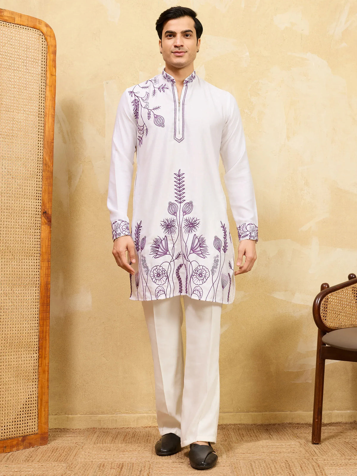 Man wearing a white ethnic kurta with purple floral embroidery and white trousers.