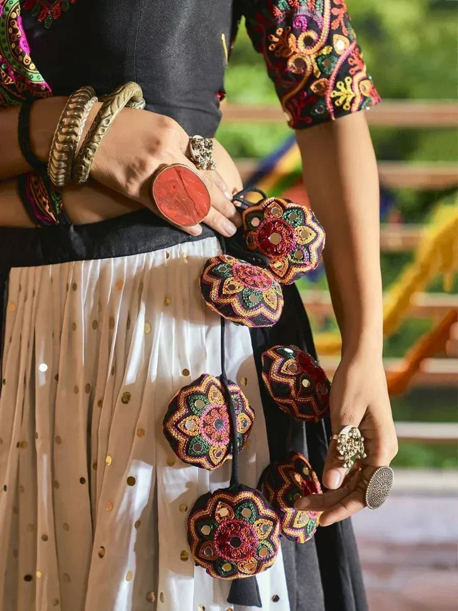 Ethnic woman in embroidered black top and gold-dotted skirt holding colorful mirror-work pouches