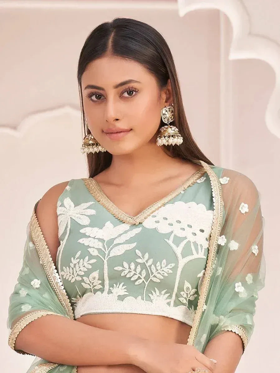 Mint green embroidered lehenga choli with white floral motifs and gold trim, paired with jhumka earrings