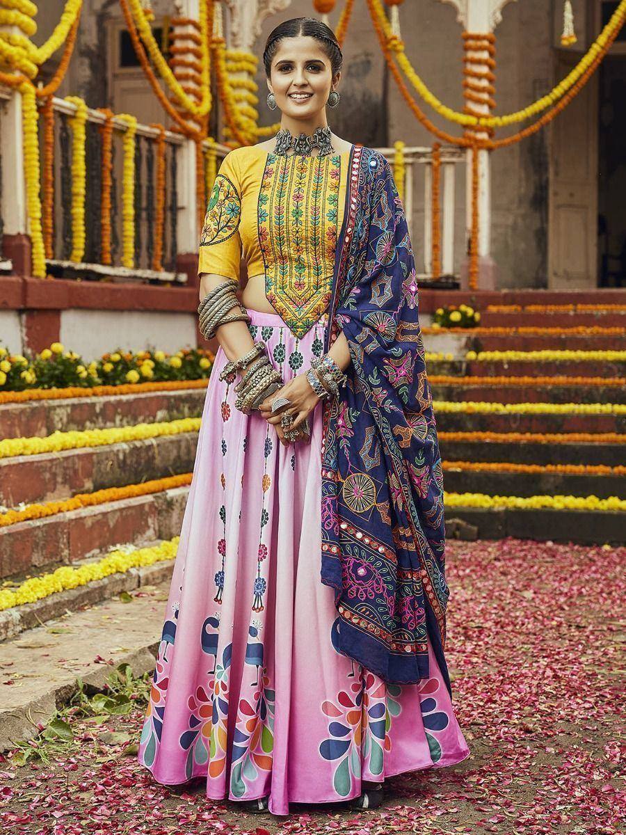 Woman in vibrant yellow and pink embroidered lehenga choli with blue dupatta, festive floral backdrop