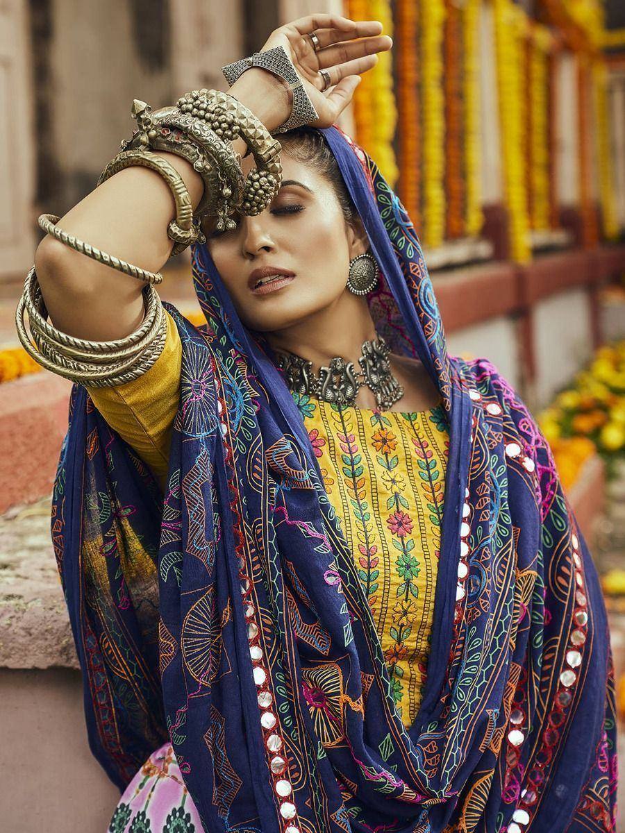 Woman in vibrant Indian ethnic wear with floral yellow top, blue embroidered dupatta, and traditional jewelry