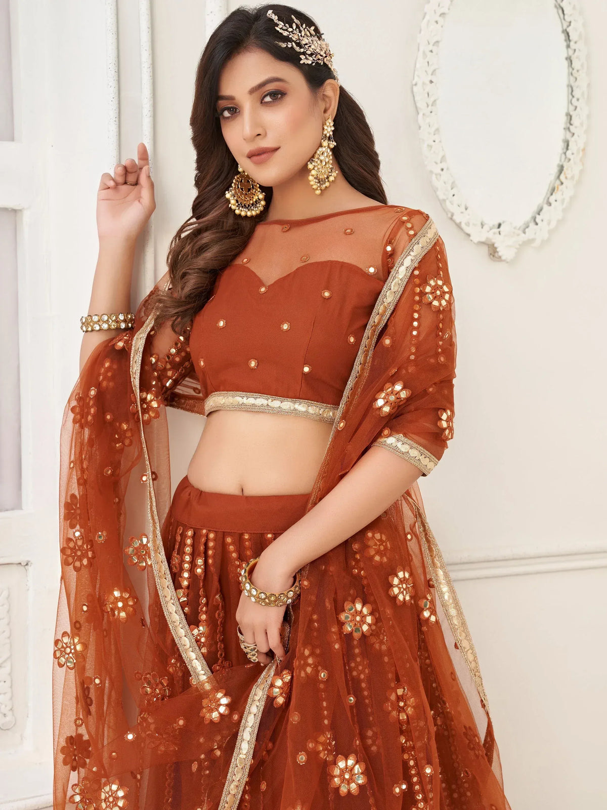 Rust orange designer lehenga choli with floral mirror work and sheer dupatta, perfect for Indian ethnic wear occasions.