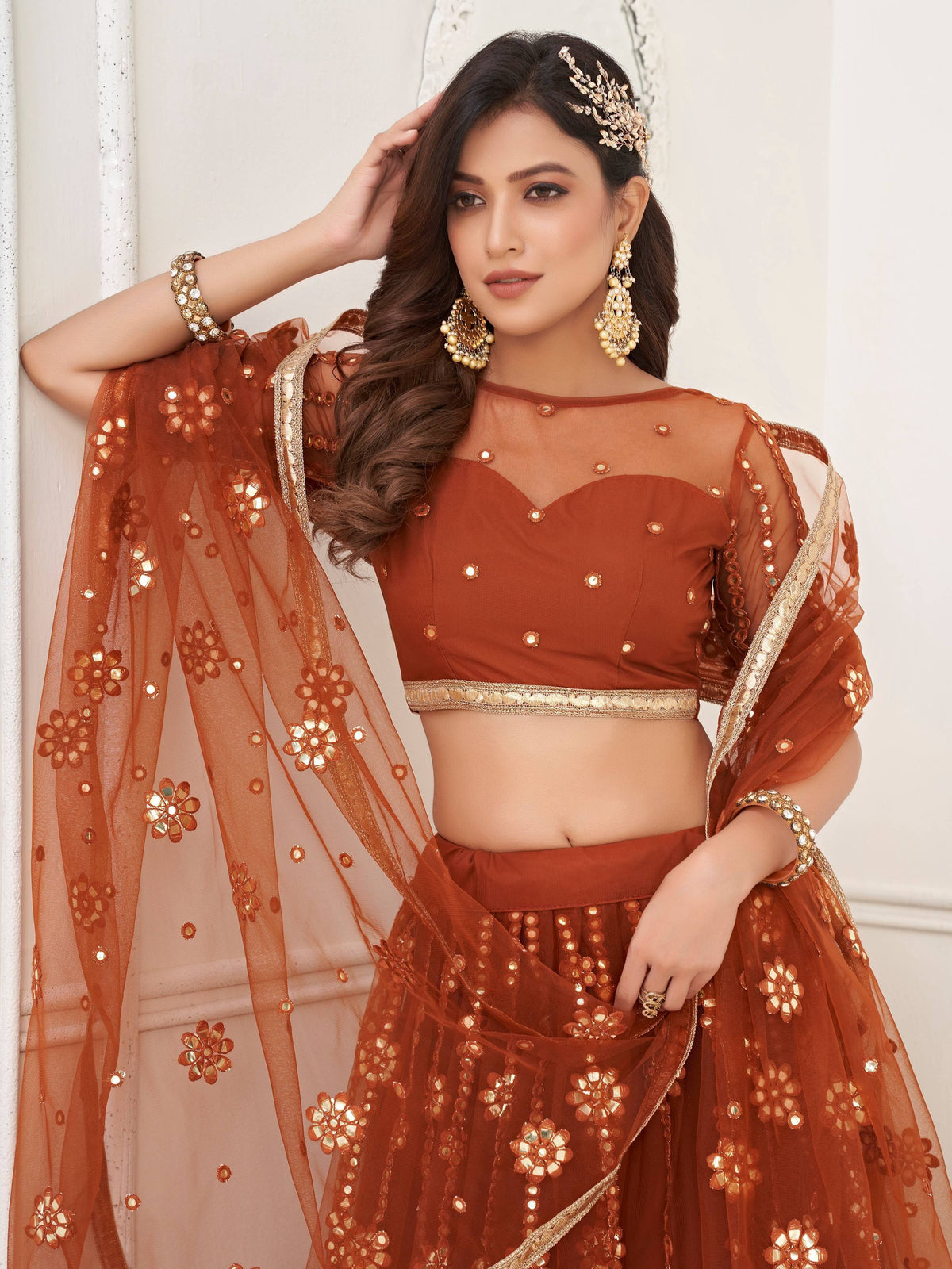 Rust-colored designer lehenga choli with floral mirror work, sheer dupatta, and gold embellishments for weddings