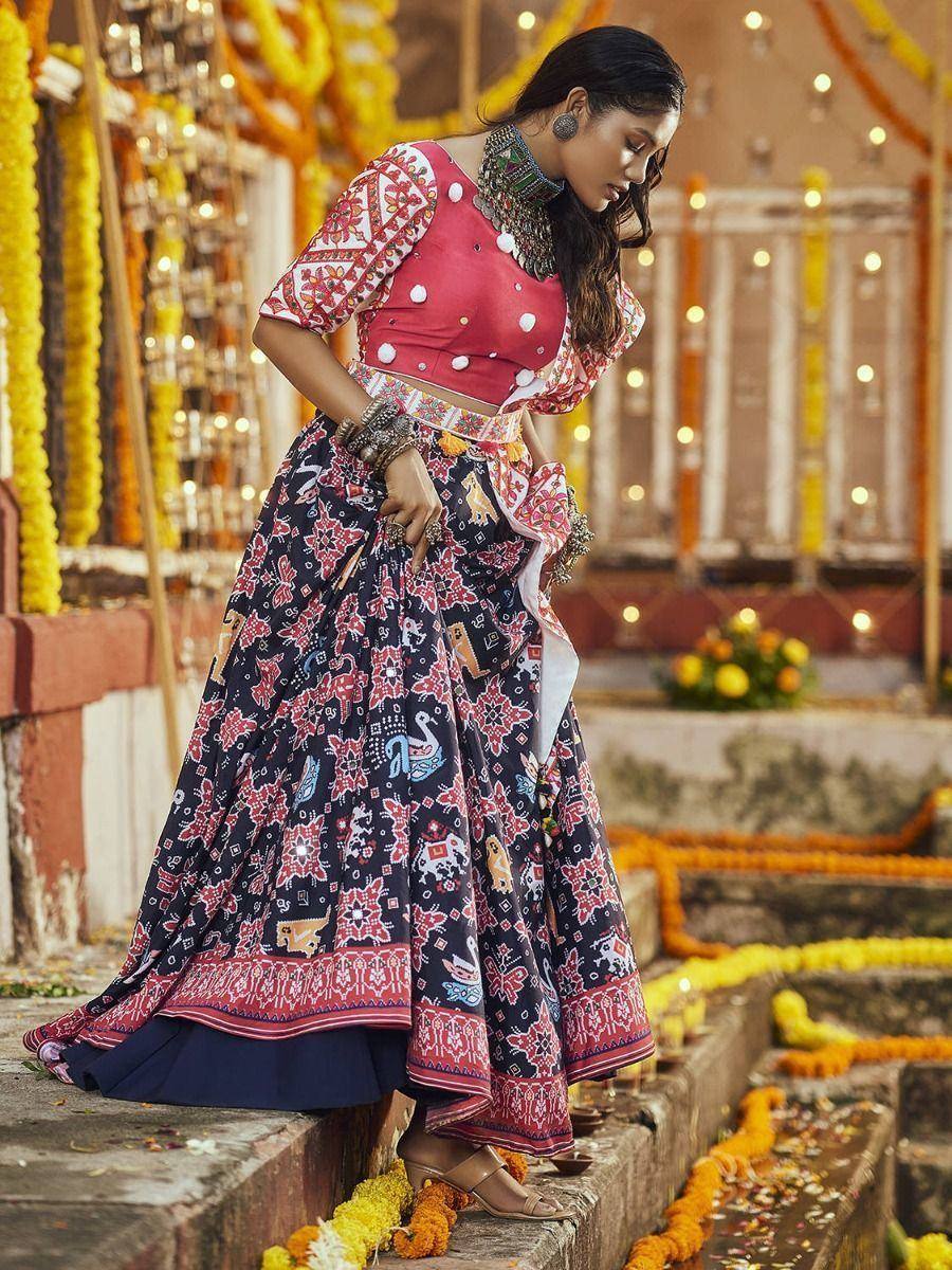 Woman in red and navy printed lehenga choli with floral motifs, festive temple backdrop
