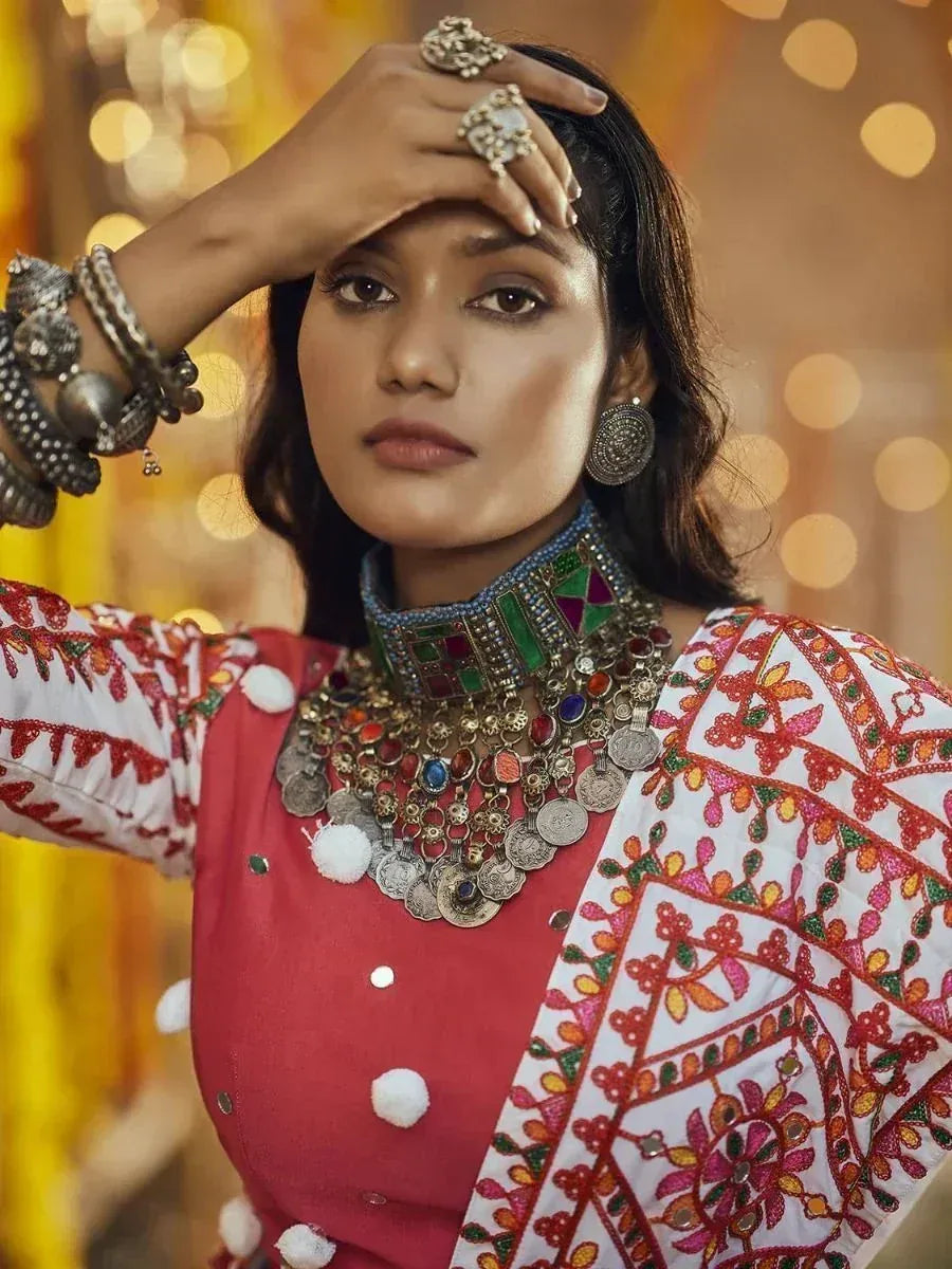 Woman in vibrant red and white embroidered ethnic wear with statement jewelry, perfect for festive occasions.