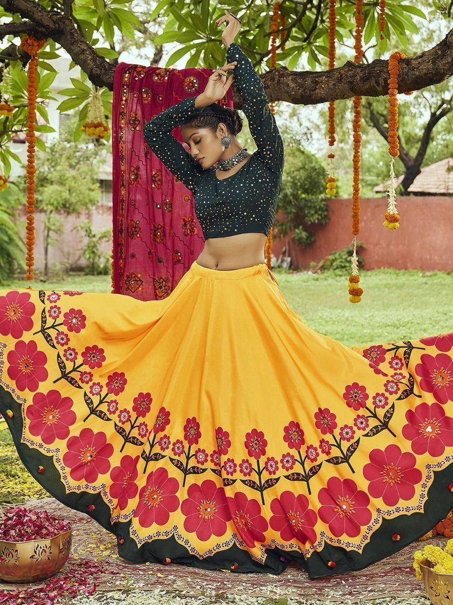 Woman in vibrant yellow floral lehenga choli with black embellished top, dancing under marigold-decorated tree