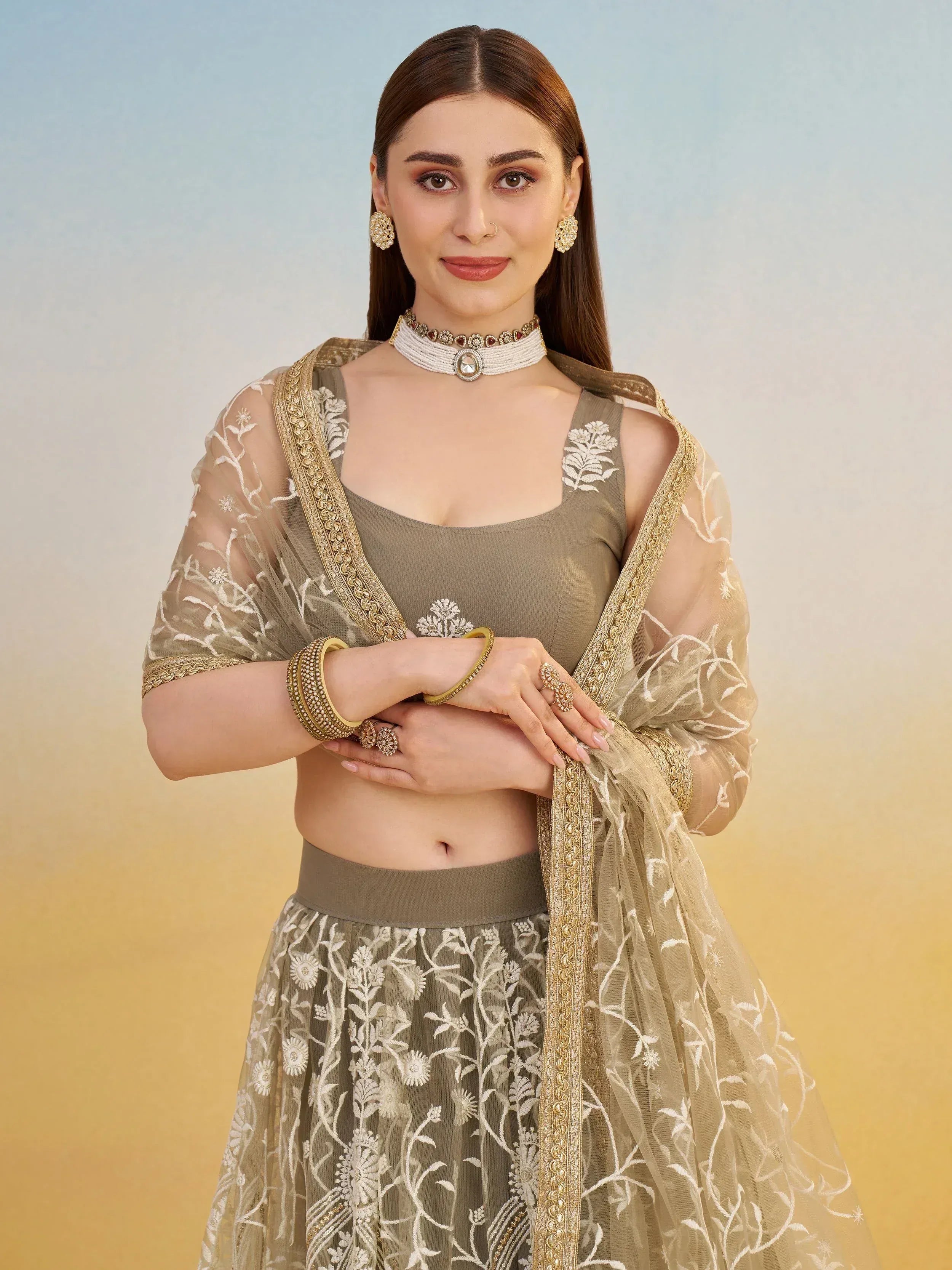 Elegant olive green lehenga choli with floral embroidery and gold trim, paired with traditional jewelry.