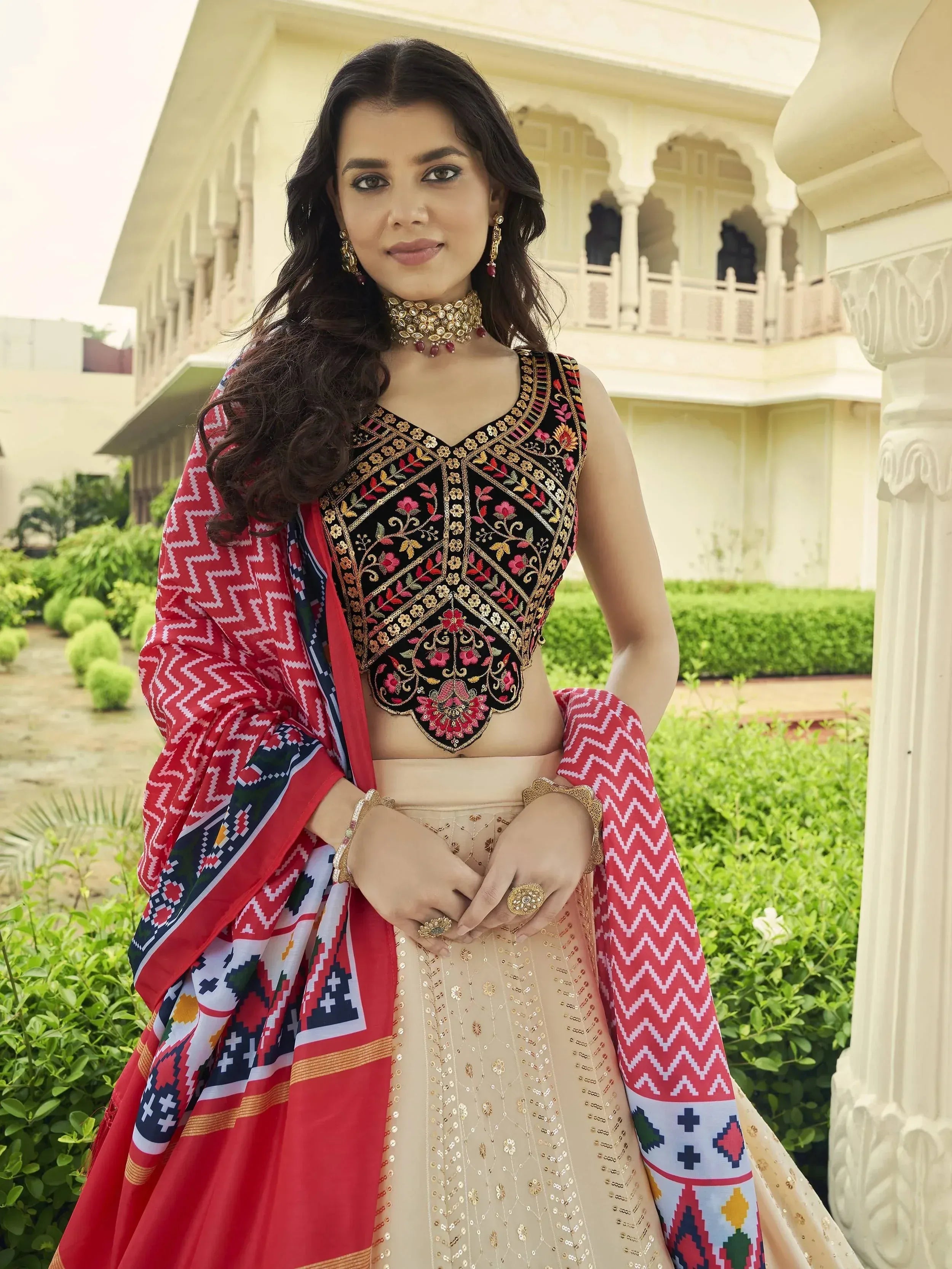 Woman in embroidered black blouse, beige lehenga, and red patterned dupatta, traditional Indian ethnic wear