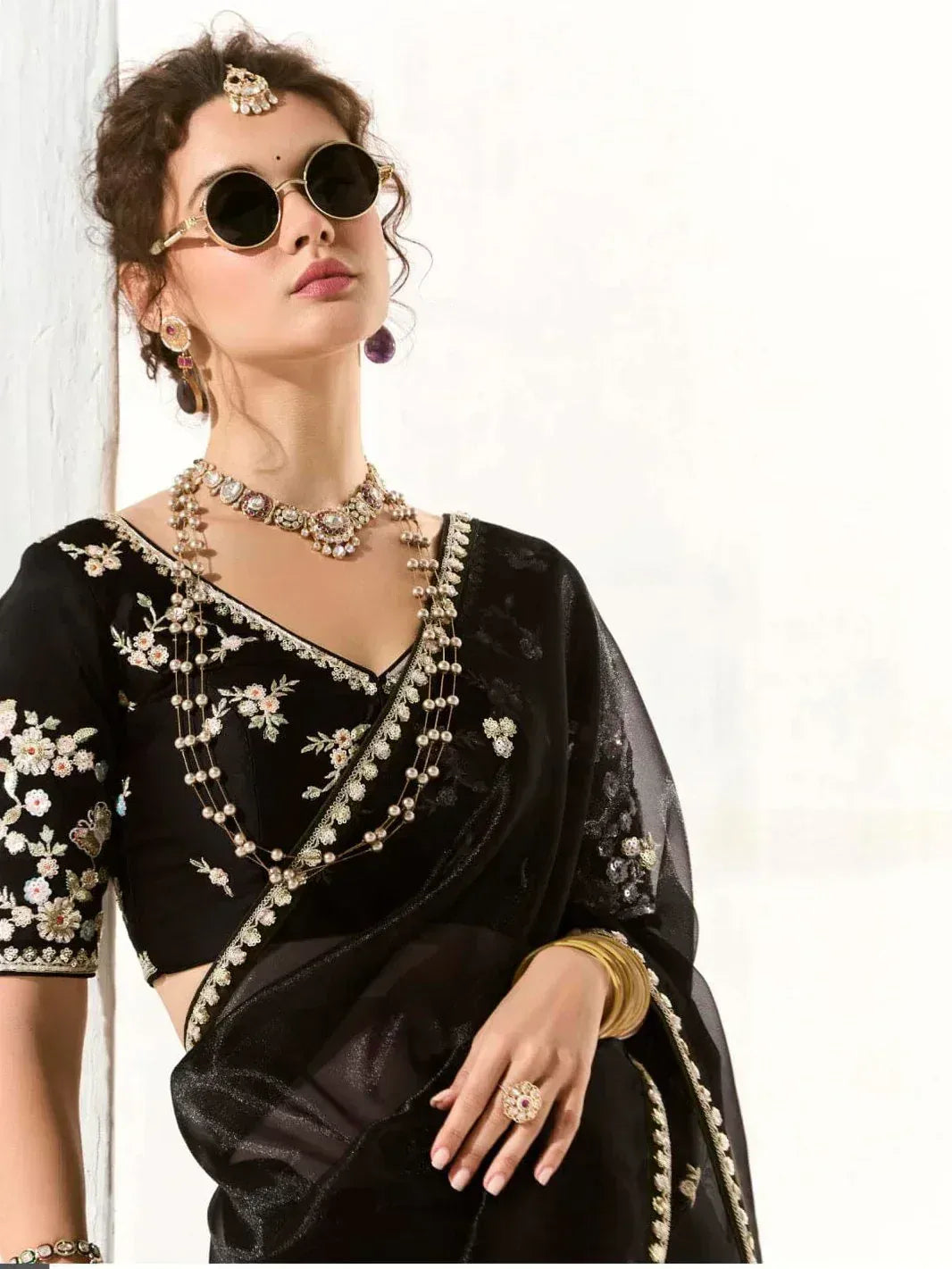 Black embroidered saree with floral detailing, statement jewelry, and round sunglasses for ethnic wear