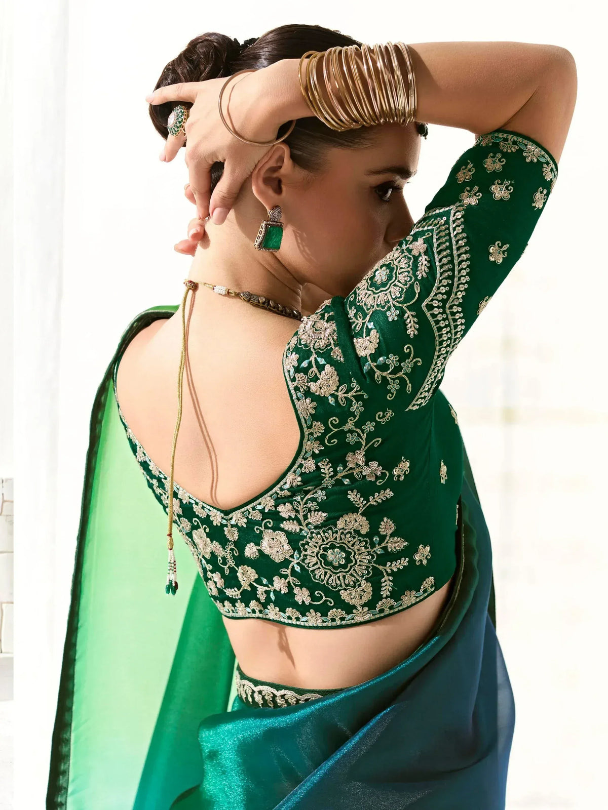 Emerald green embroidered saree blouse with floral zari work, backless design, and gold bangles