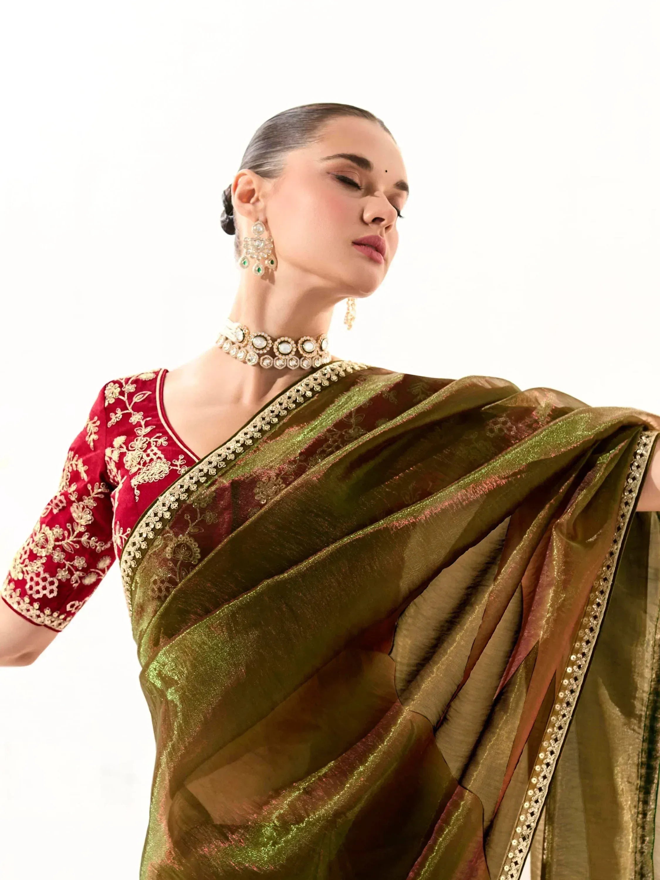 Elegant woman in olive green saree with red embroidered blouse, gold jewelry, perfect for Indian ethnic wear occasions.