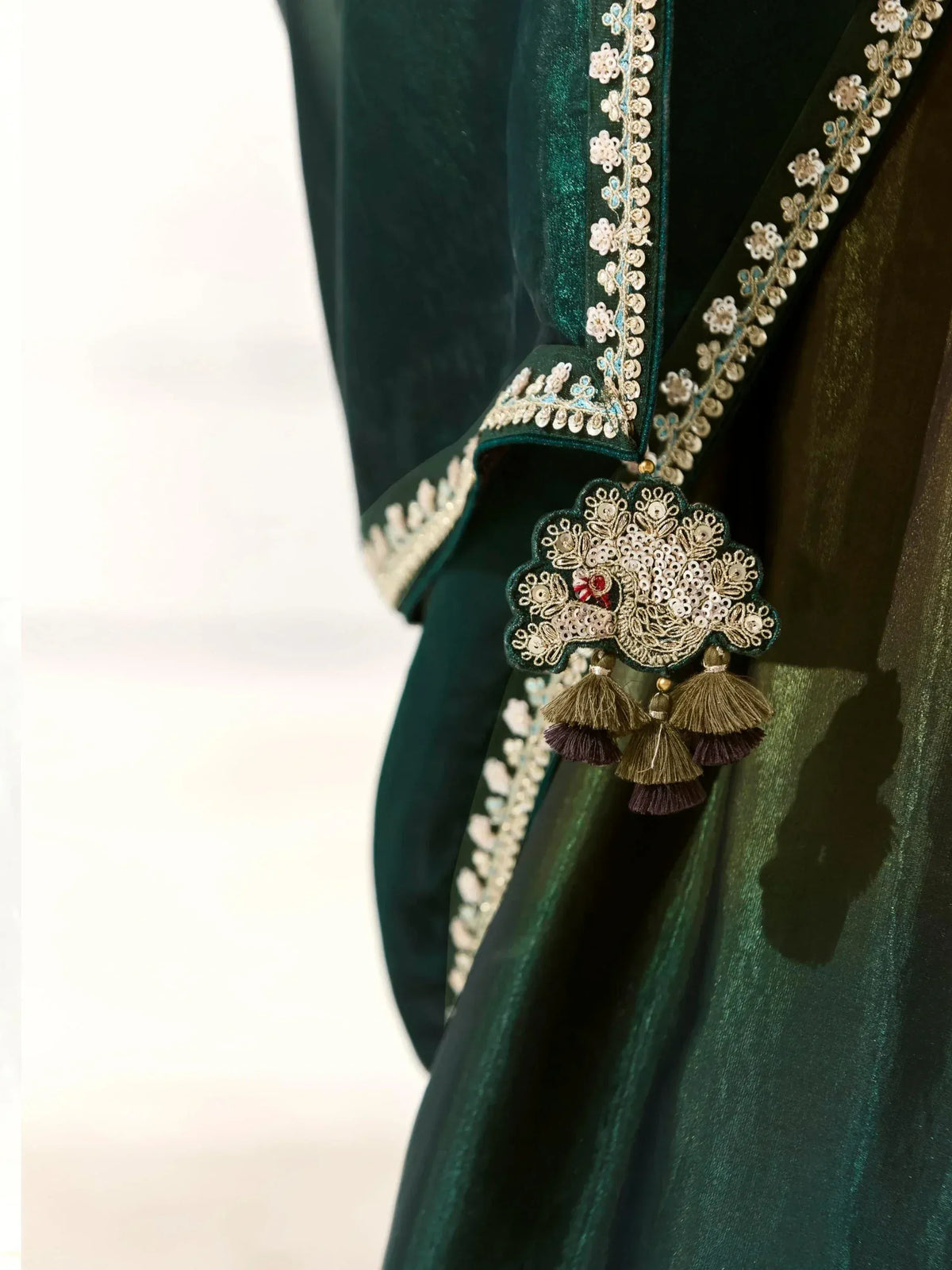 Emerald green velvet ethnic wear with intricate gold embroidery and tassels, perfect for festive occasions.