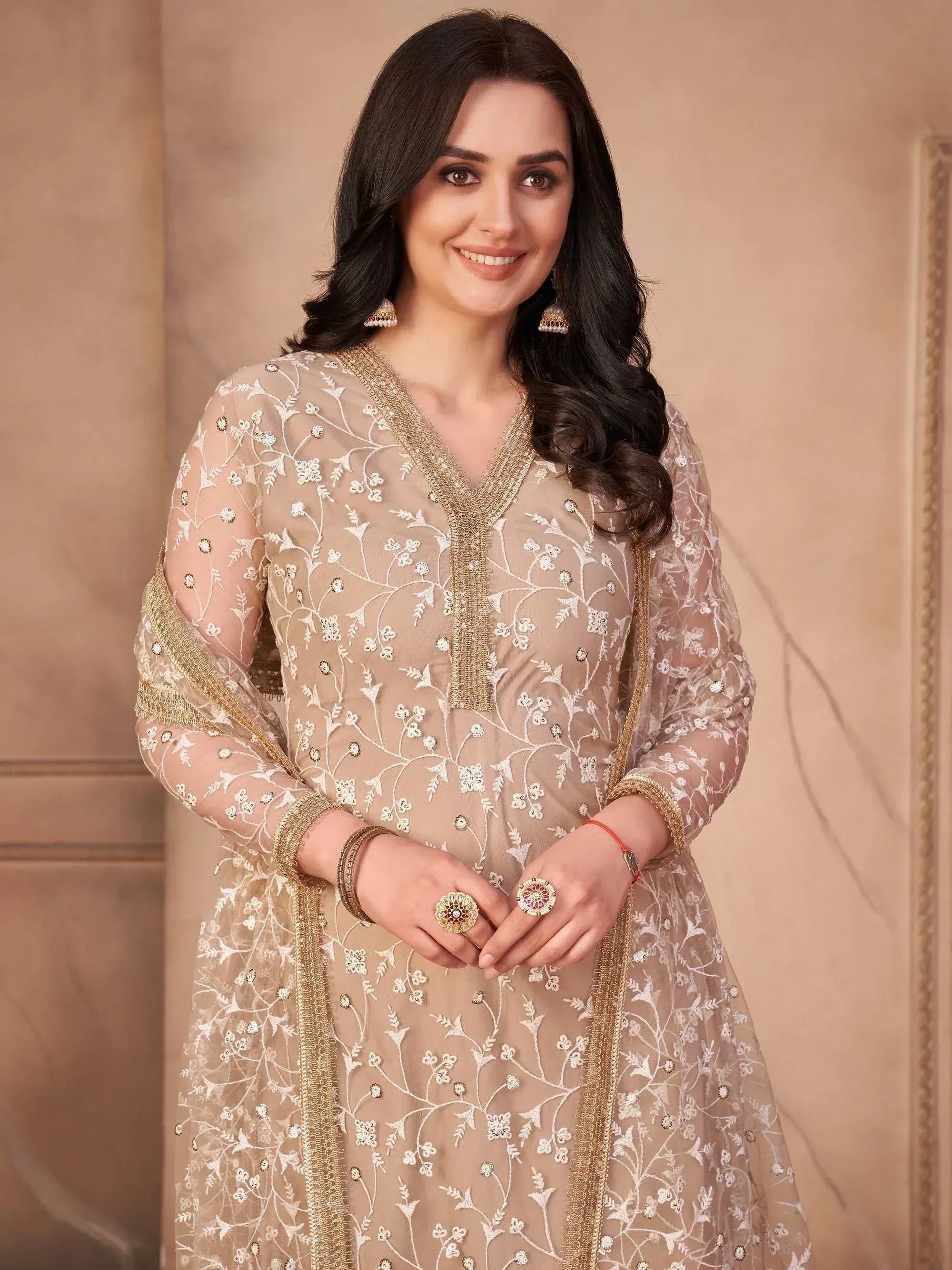 Woman in beige embroidered salwar kameez with dupatta, wearing ethnic jewelry