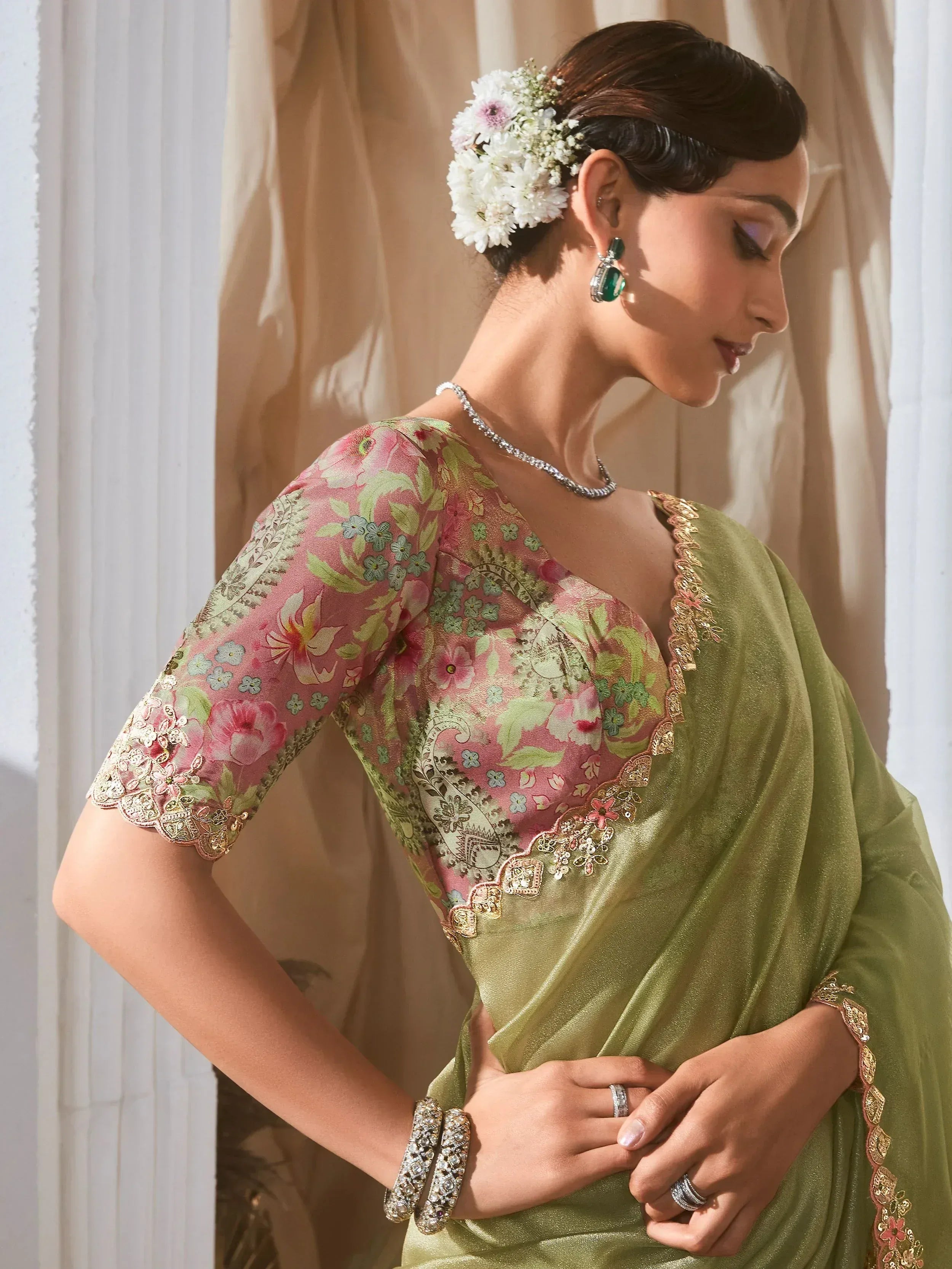 Elegant woman in olive green saree with floral pink blouse, gold embroidery, and floral hair accessory