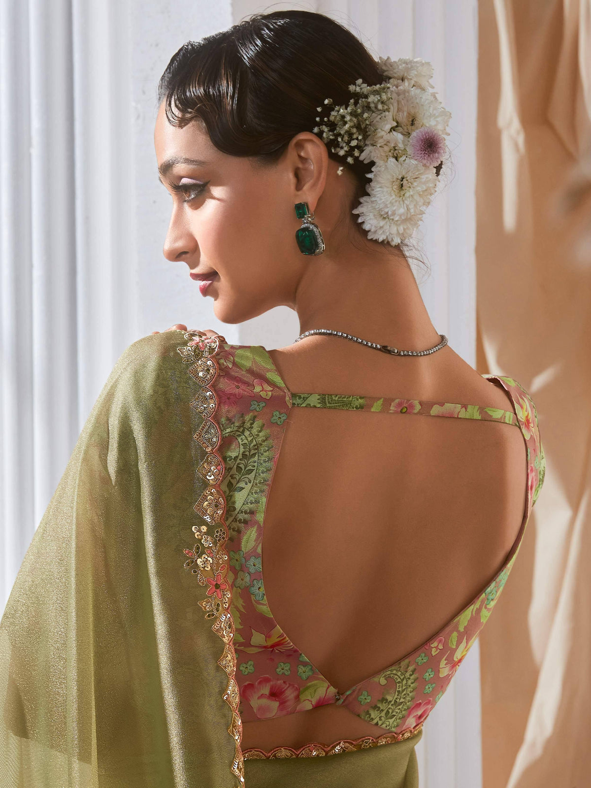 Woman in floral print backless saree blouse with gold embroidery, emerald earrings, and floral hair accessory
