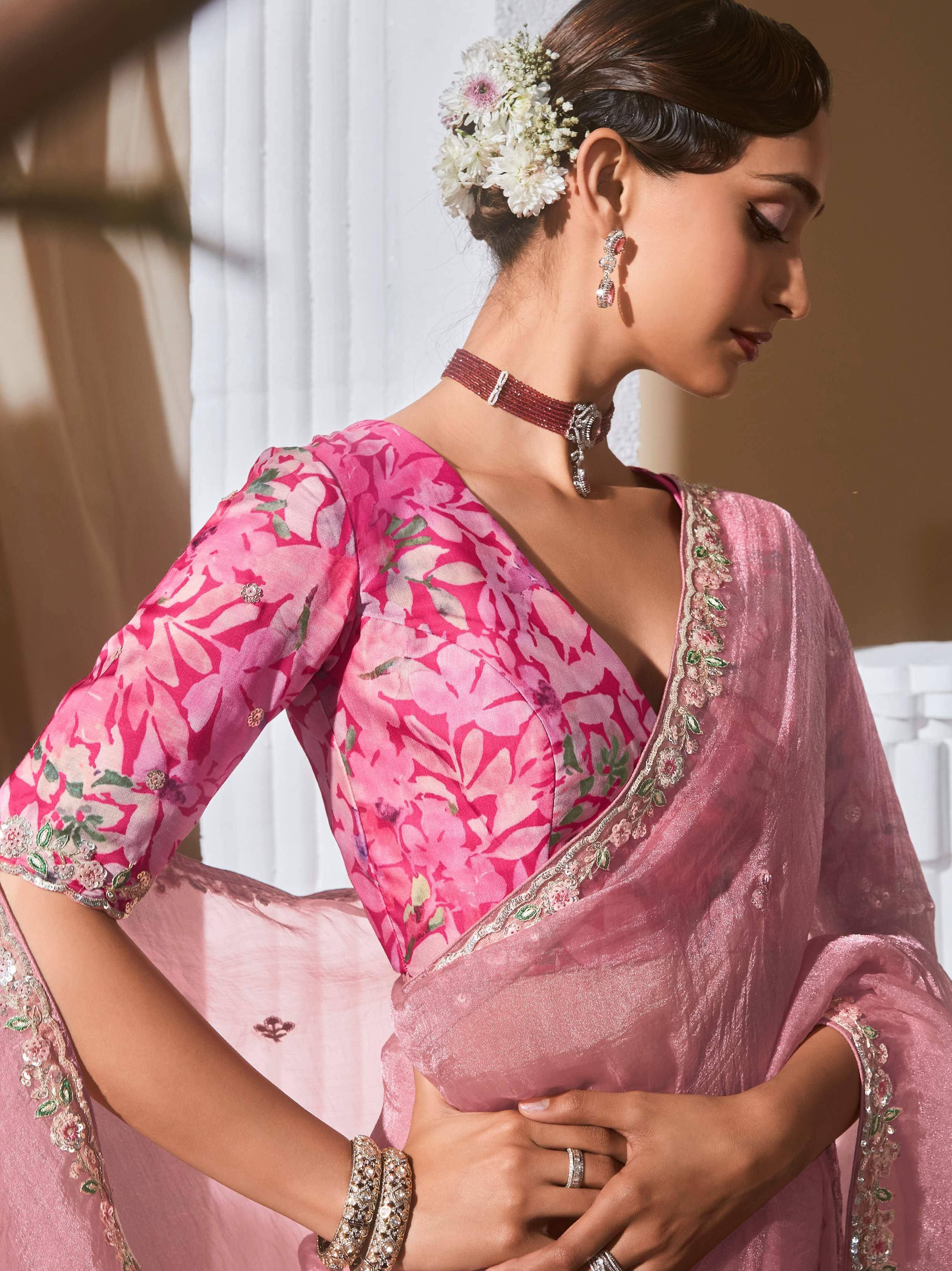 Pink floral printed designer saree with embroidered border and matching blouse, styled with floral hair accessory