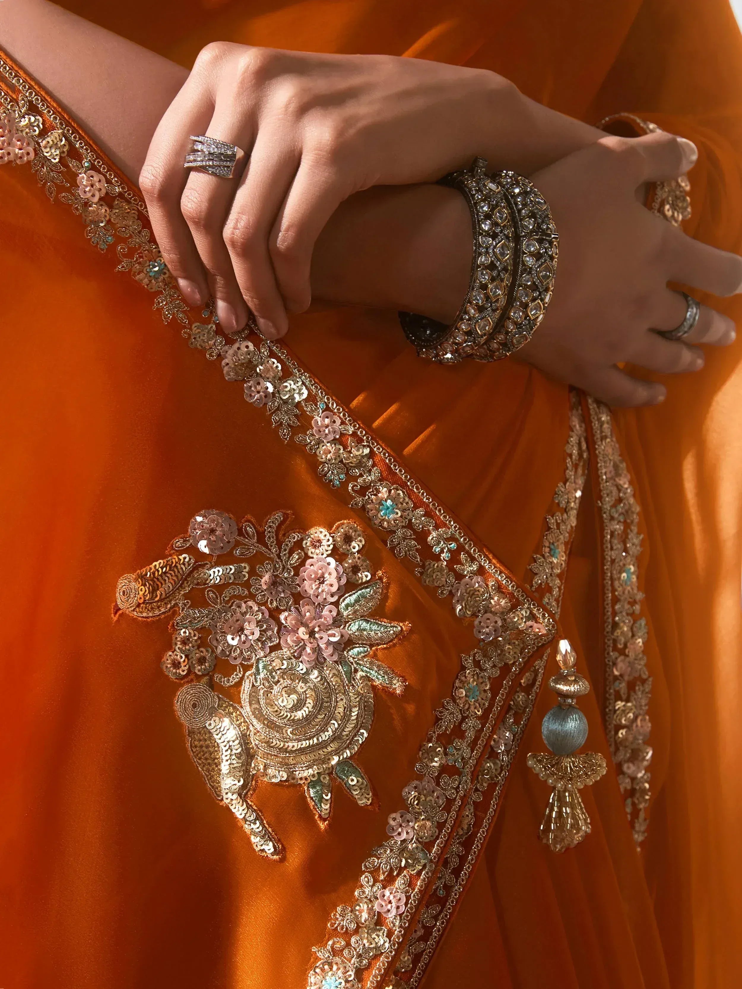 Orange ethnic saree with floral sequin embroidery, gold border, and traditional jewelry